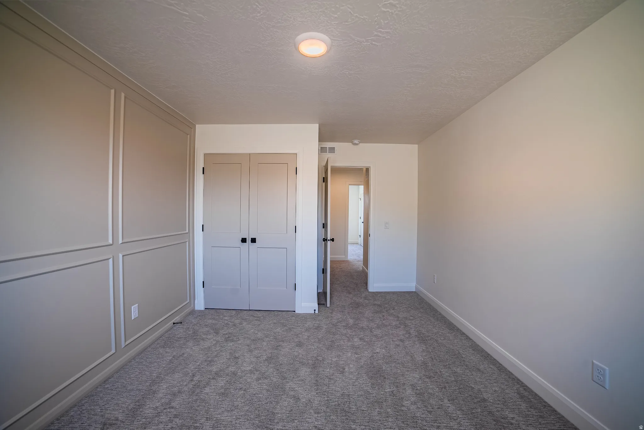 Bedroom featuring wainscoting accent wall, gray carpet flooring, flush mount ceiling light, and panel doors with black hardware