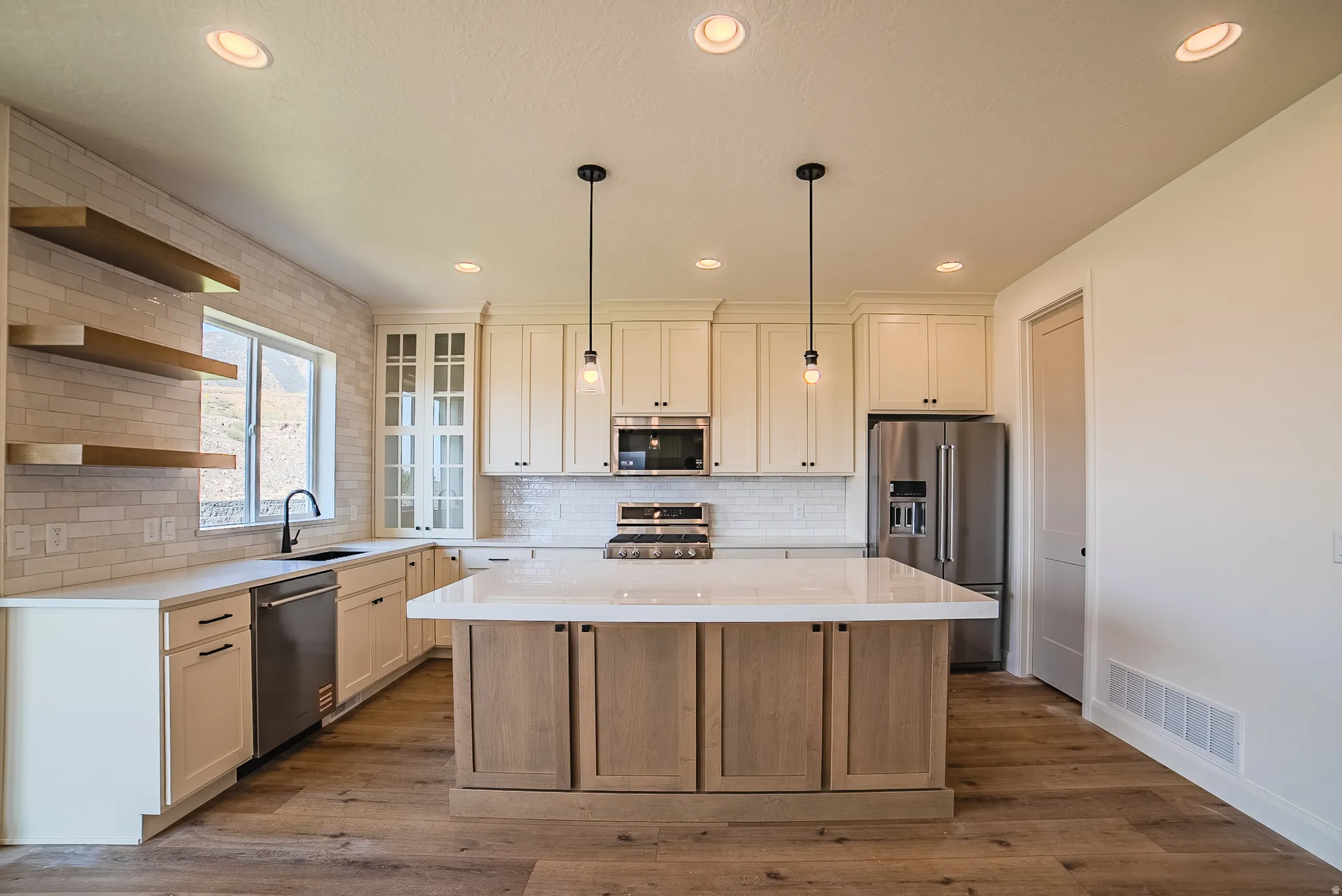 Kitchen featuring a large central island with seating, pendant lighting, stainless steel appliances, a subway tile backsplash, and wood-finish flooring