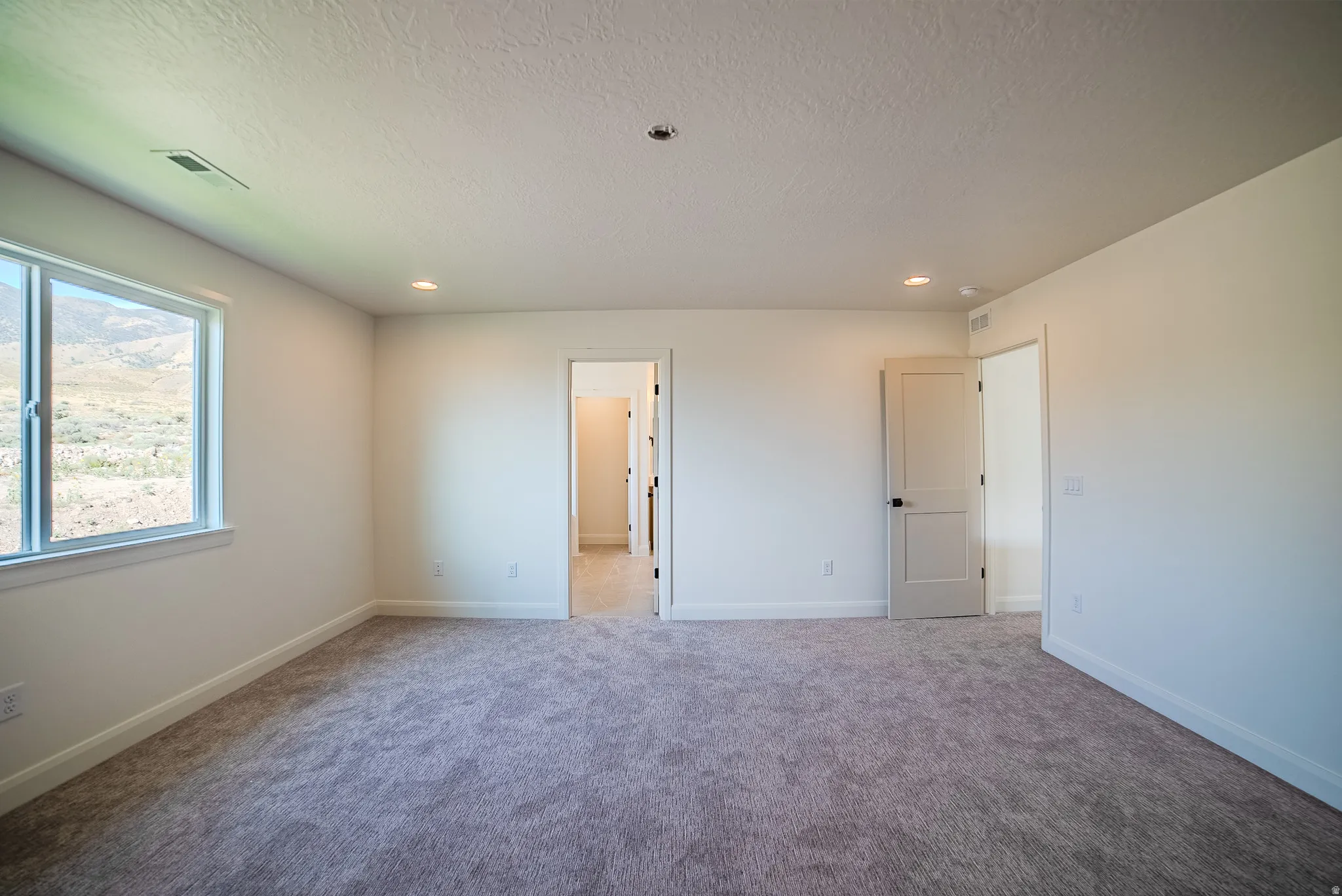 Spacious room featuring neutral carpeting, recessed lighting, and a large window providing expansive outdoor scenery