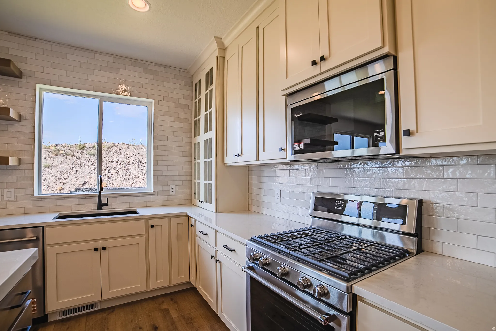 Kitchen featuring stainless steel gas range, built-in microwave, light-toned cabinetry, subway tile backsplash, and light countertops