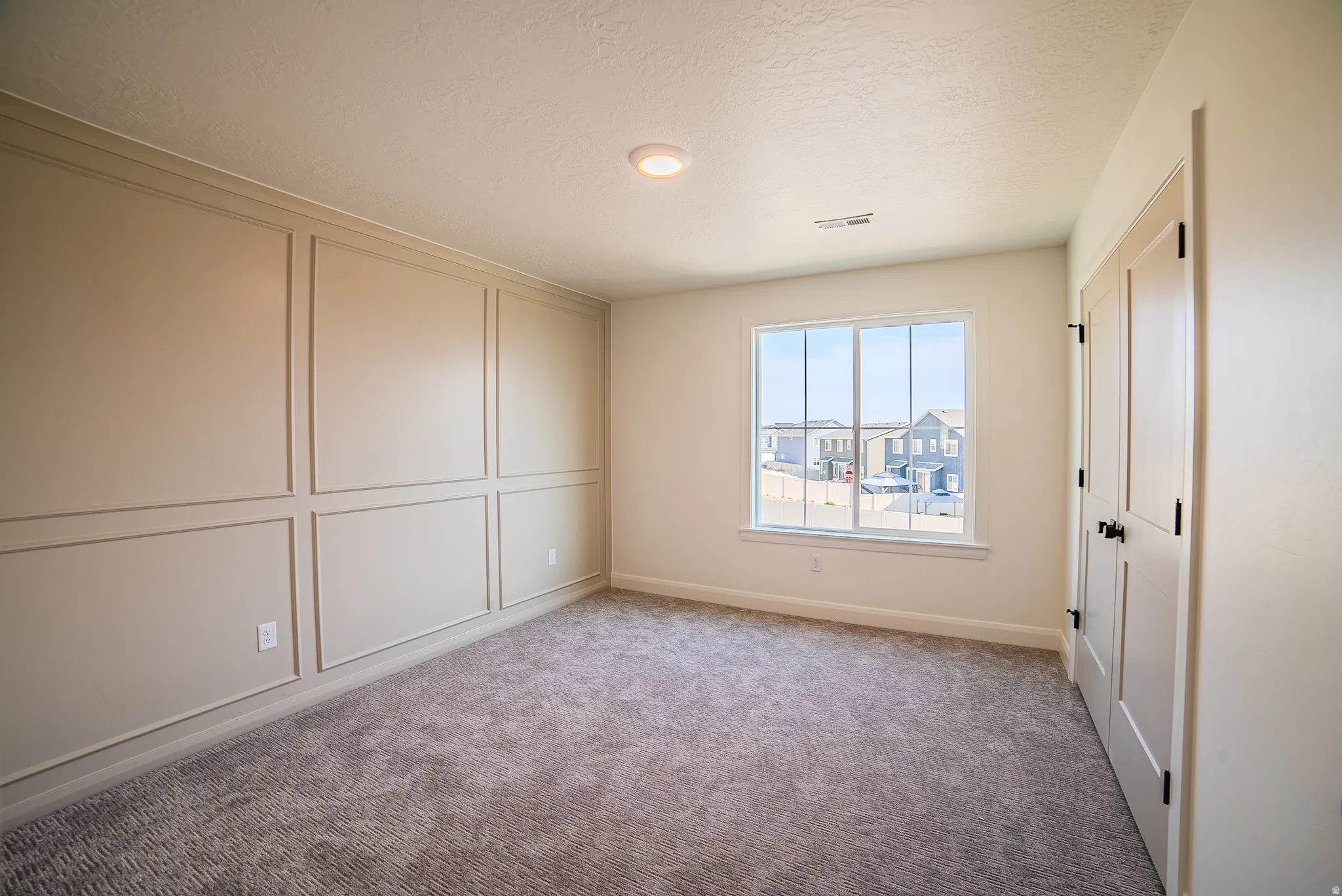Carpeted room featuring a window with white trim, a decorative panel accent wall, and a flush-mount ceiling light
