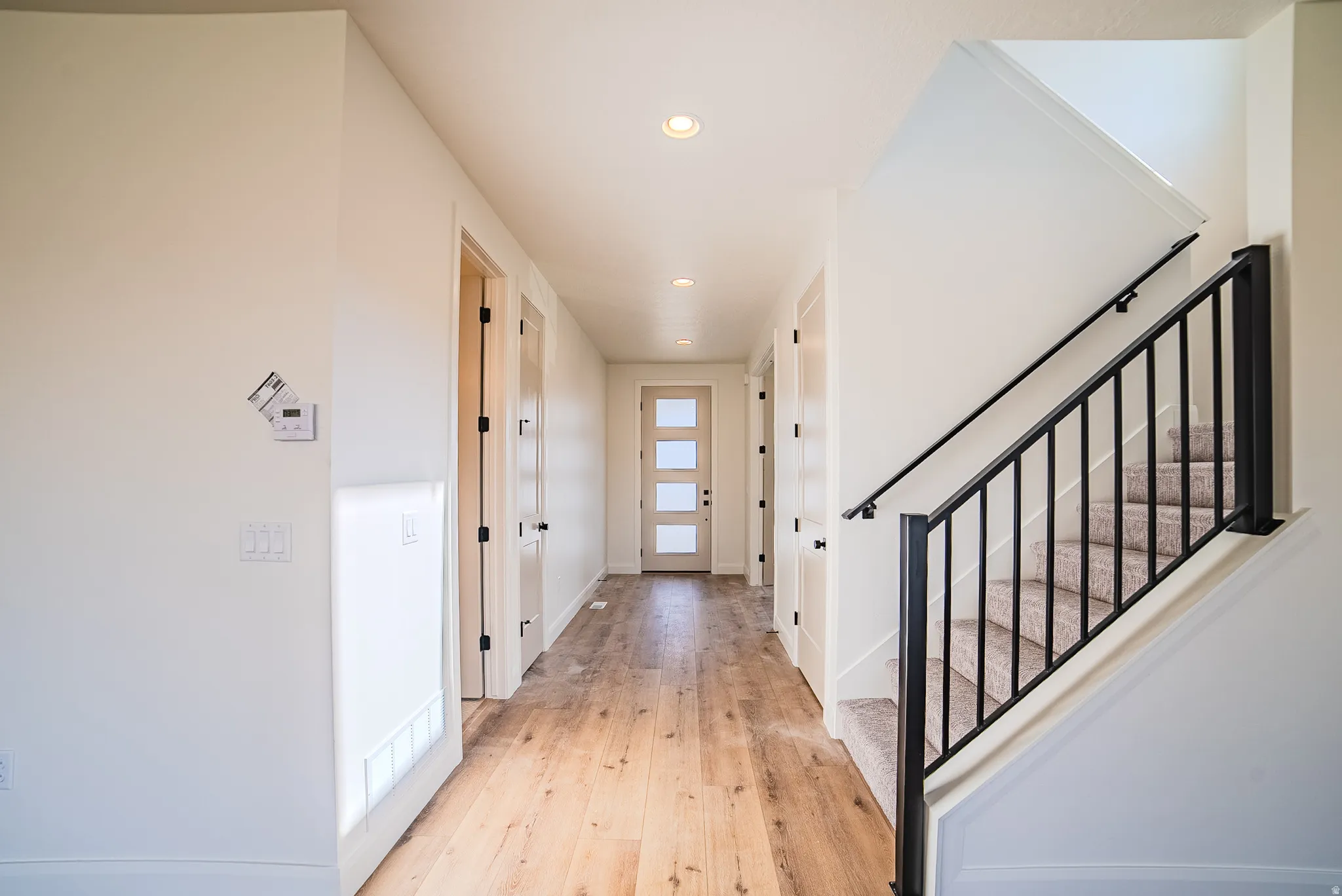 Expansive hallway featuring wood-finish flooring, recessed lighting, and a contemporary front door with frosted glass panels