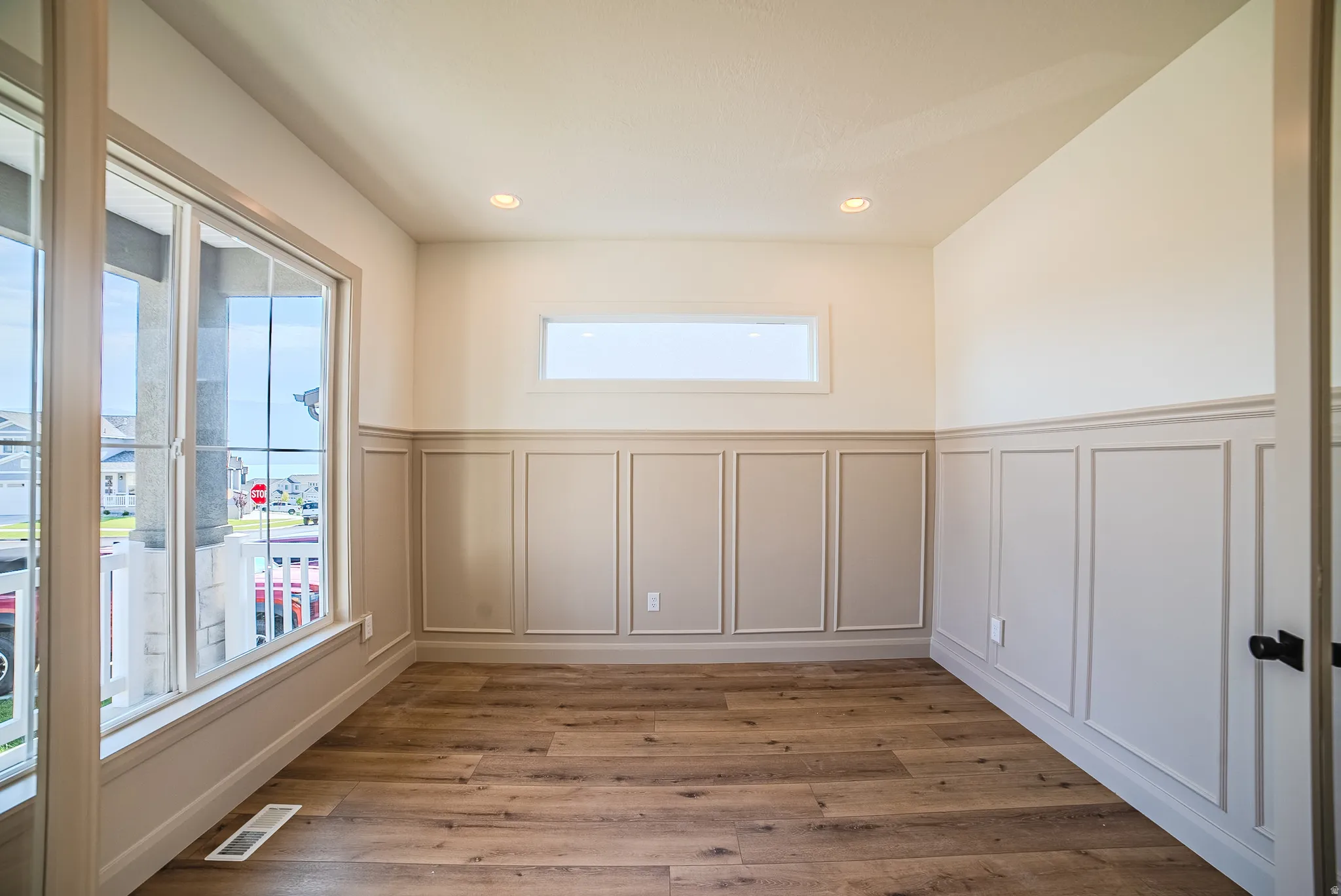 Room featuring wood-finish flooring, wainscoting paneling, recessed lighting, and a transom window