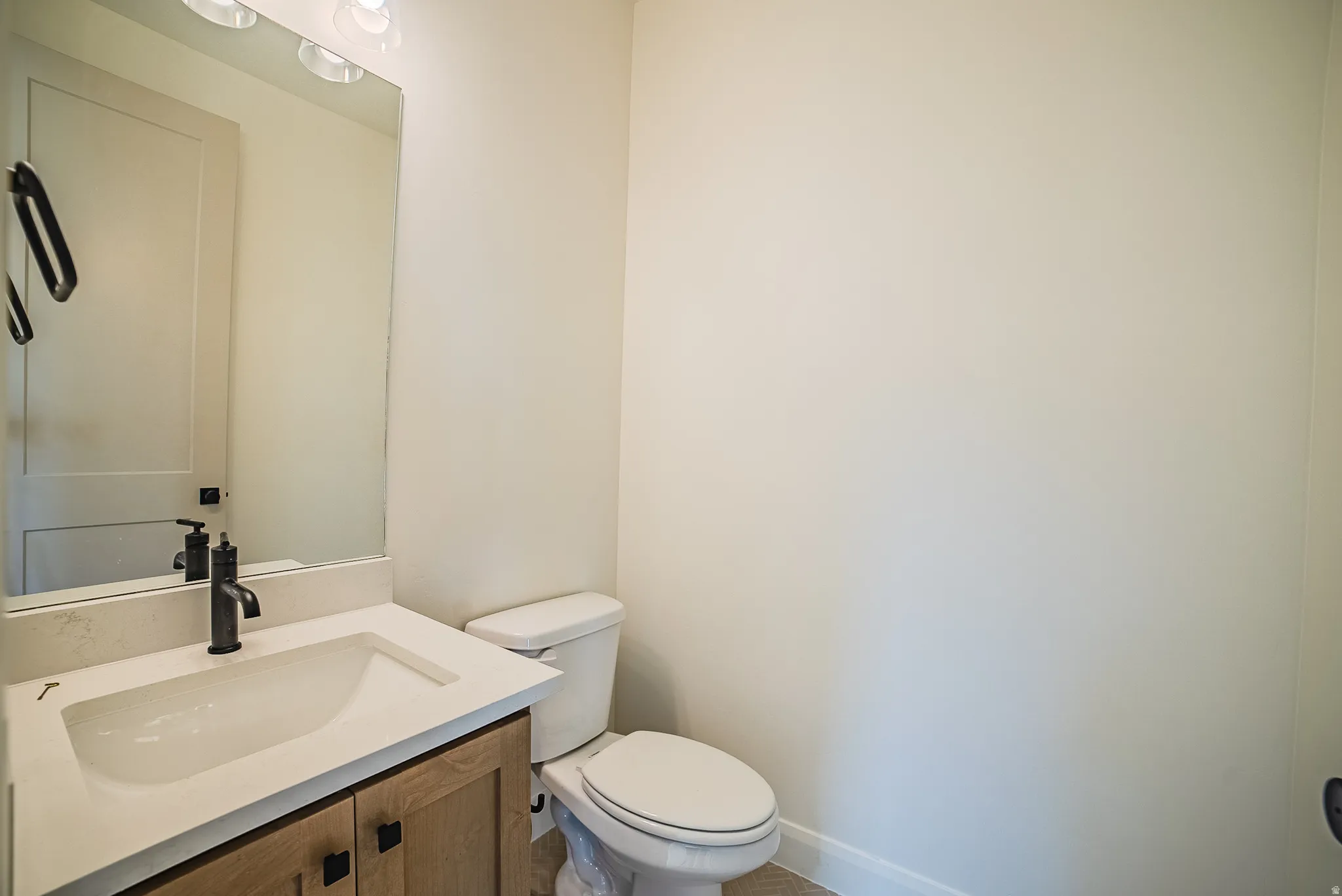 Bathroom vanity featuring a light wood-finish base with matte black hardware, integrated sink, and light-toned countertop