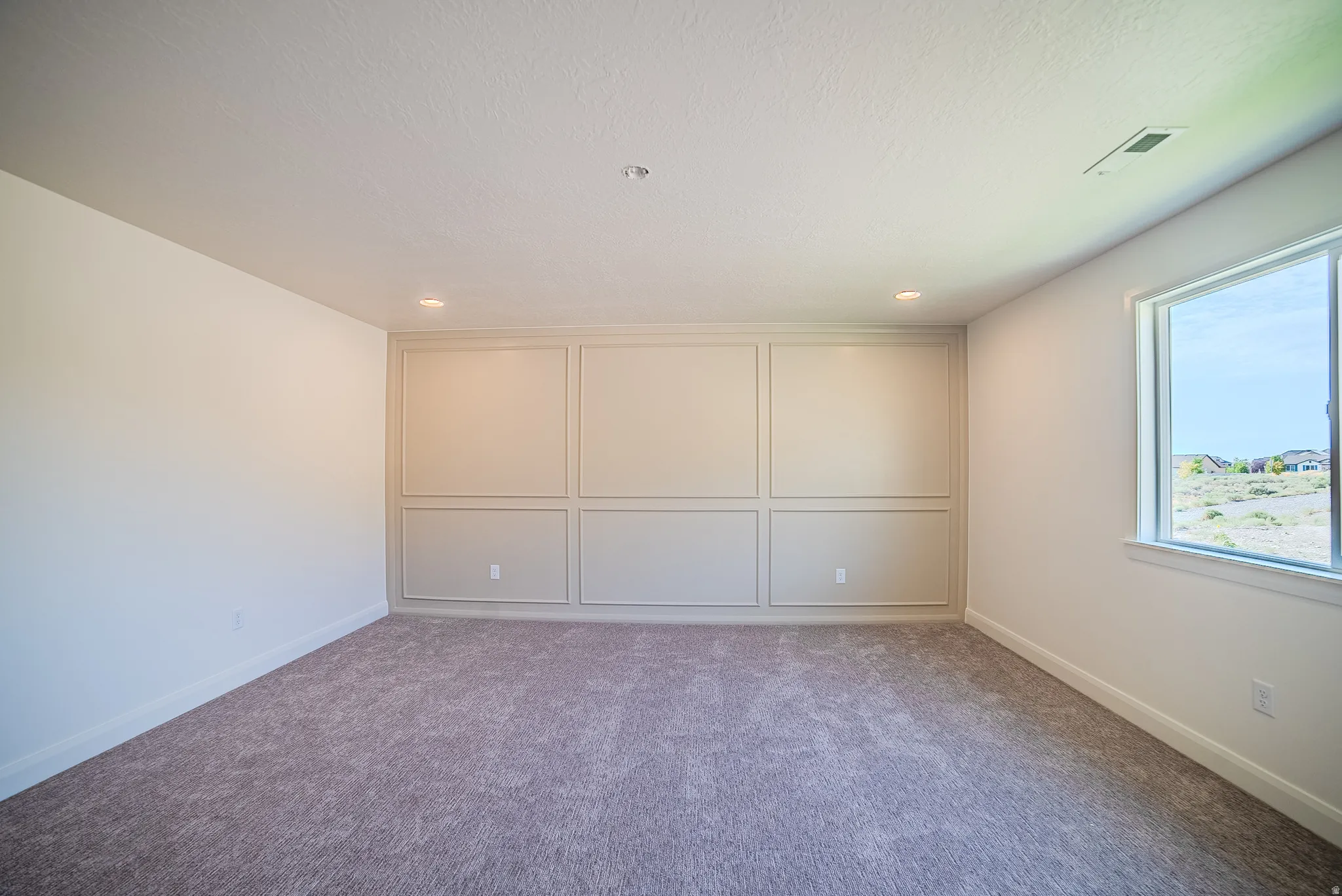 Spacious room featuring accent wall paneling, recessed lighting, neutral tone carpet flooring, a large window, and white trim