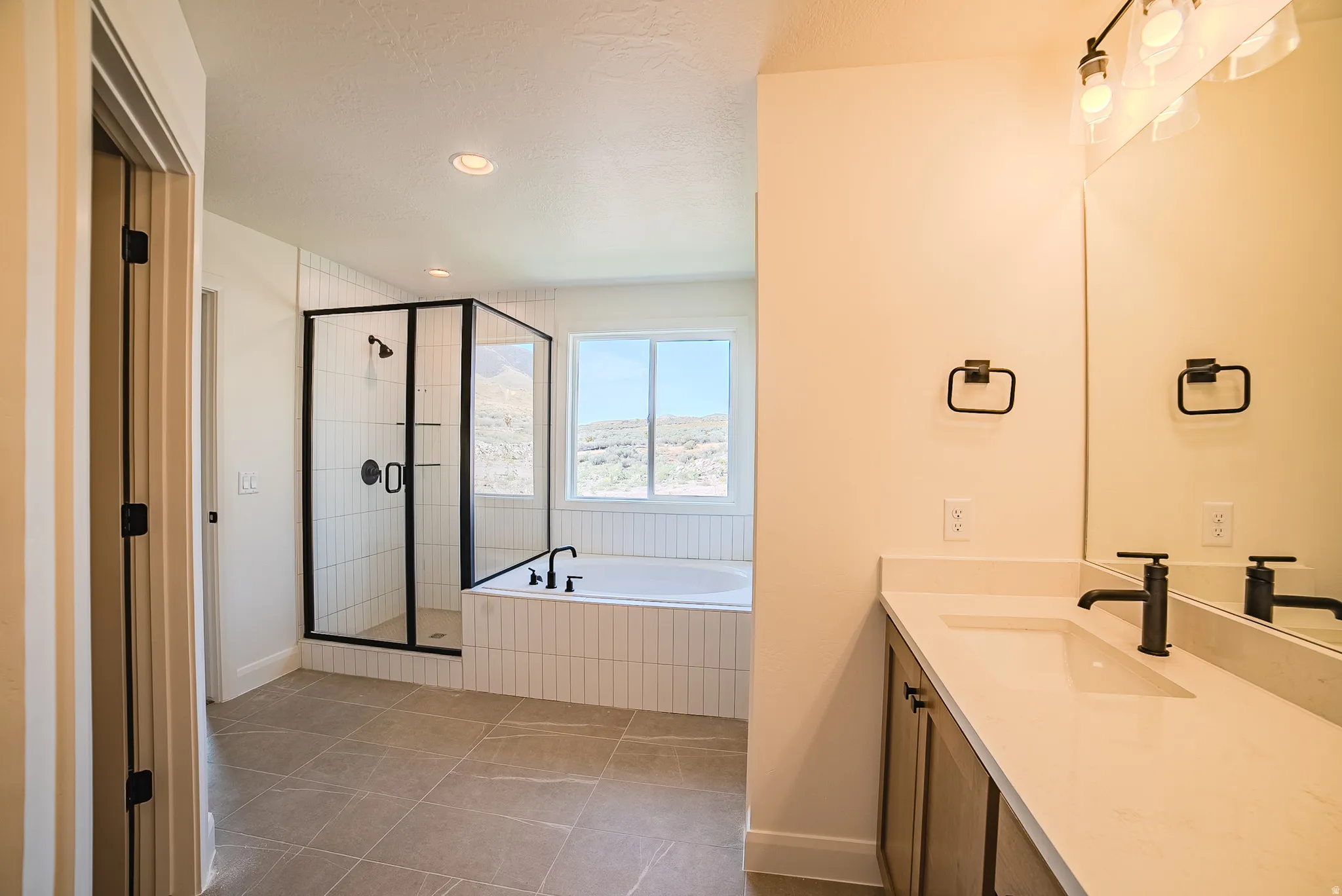 Modern bathroom with tile flooring featuring a glass-enclosed shower with black framing, a built-in soaking tub, a double vanity with stone countertops, and matte black fixtures