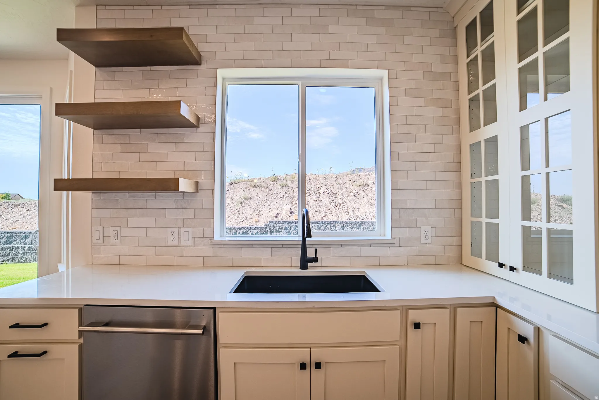 Kitchen featuring a subway tile backsplash, white countertops, a black rectangular sink with a matte black faucet, and white cabinetry with glass-front doors