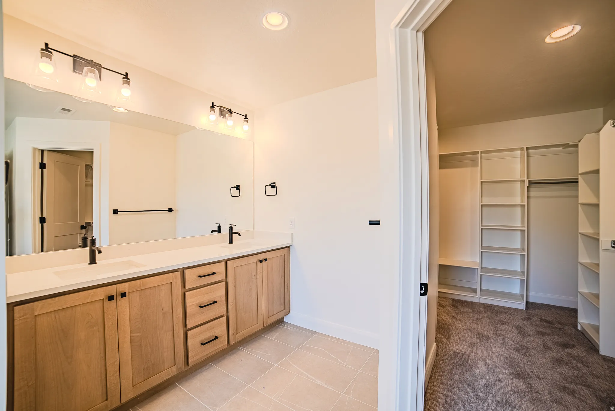 Dual vanity with light wood-finish cabinetry, white countertop, and matte black fixtures