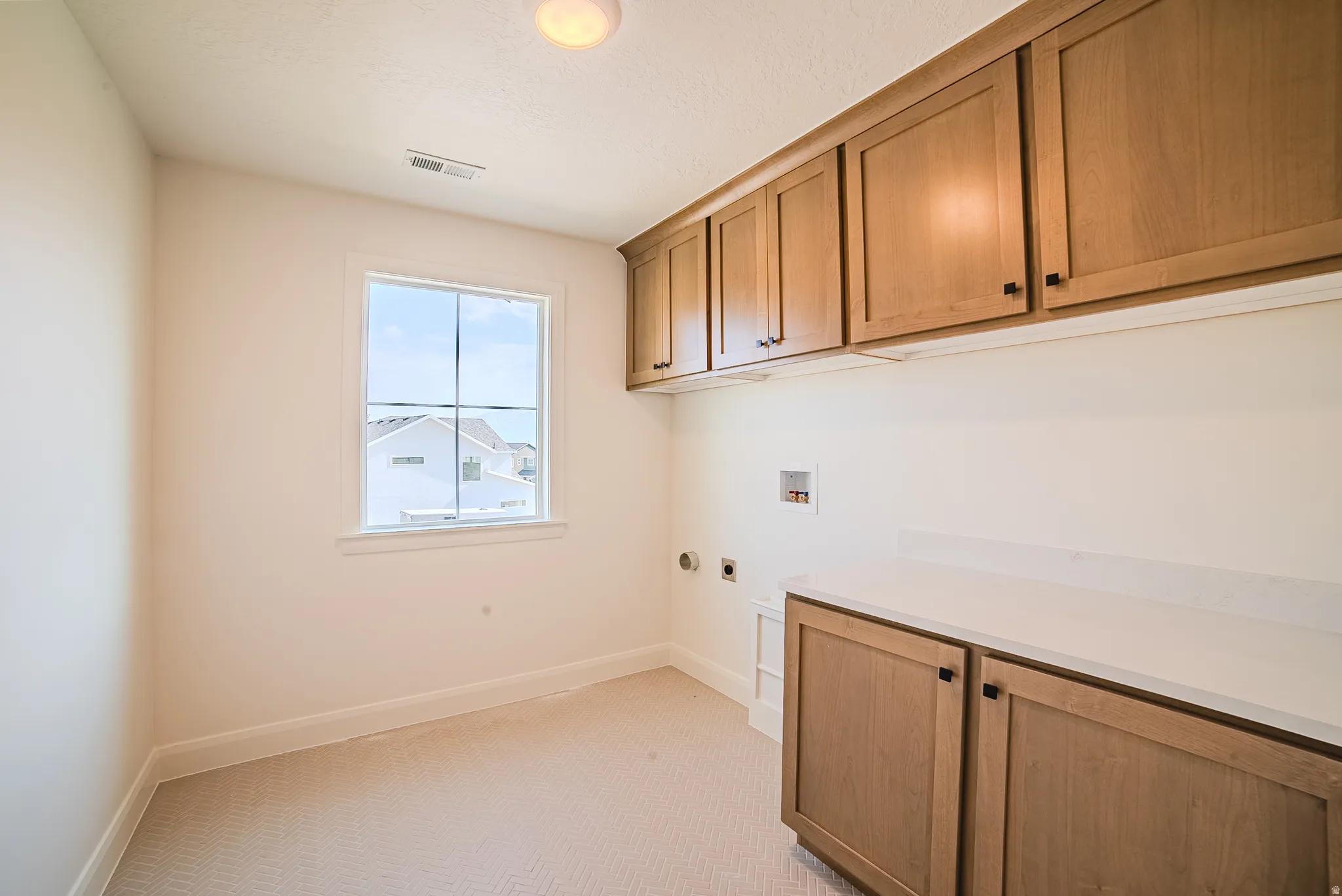 Utility room featuring natural wood cabinetry, light-toned countertops, and a single window
