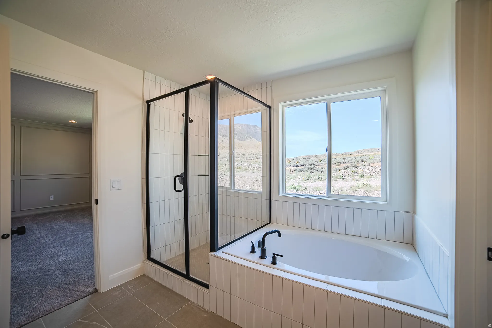 Contemporary bathroom featuring a freestanding tub, separate glass-enclosed shower with black framing, and a window with a mountain backdrop