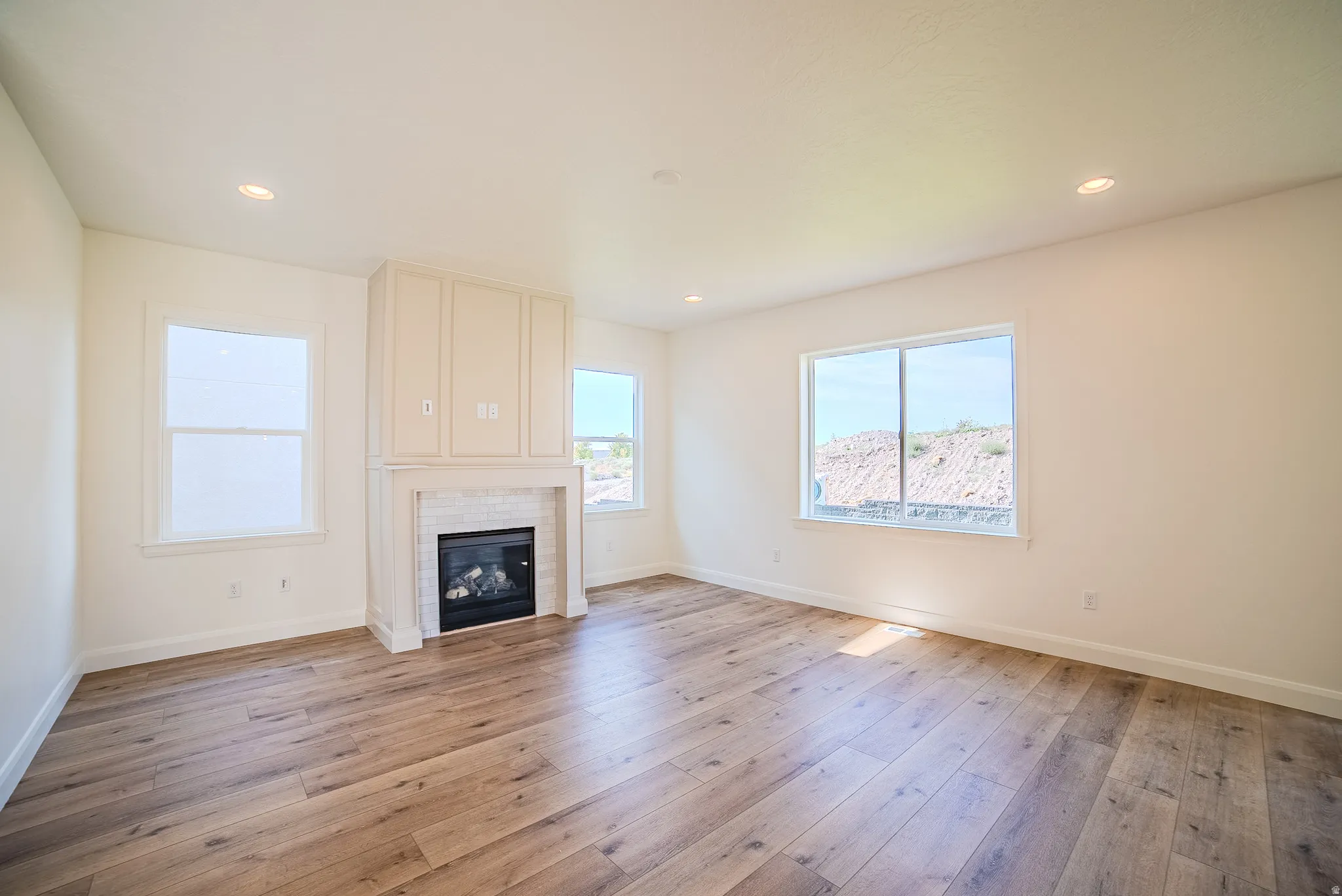 Spacious room featuring wood-finish flooring, a contemporary fireplace with subway tile surround and built-in cabinetry, recessed lighting, and multiple windows