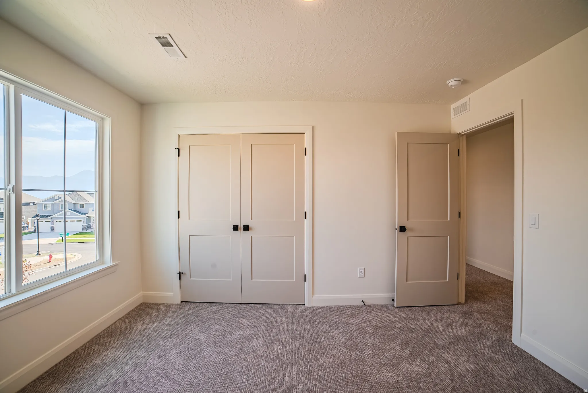 Spacious room featuring neutral carpeting, a large window with white framing, and two panel doors with black hardware
