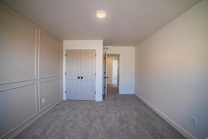 Bedroom featuring wainscoting accent wall, gray carpet flooring, flush mount ceiling light, and panel doors with black hardware