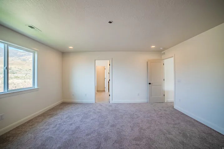 Spacious room featuring neutral carpeting, recessed lighting, and a large window providing expansive outdoor scenery