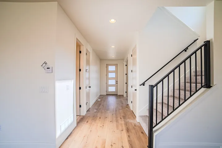 Expansive hallway featuring wood-finish flooring, recessed lighting, and a contemporary front door with frosted glass panels