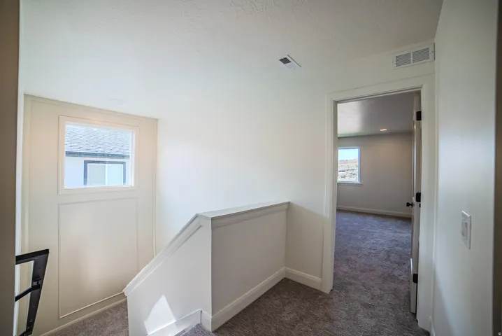 Upper-level landing featuring a window, painted white trim, white baseboards, and plush grey carpeting