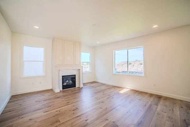 Spacious room featuring wood-finish flooring, a contemporary fireplace with subway tile surround and built-in cabinetry, recessed lighting, and multiple windows