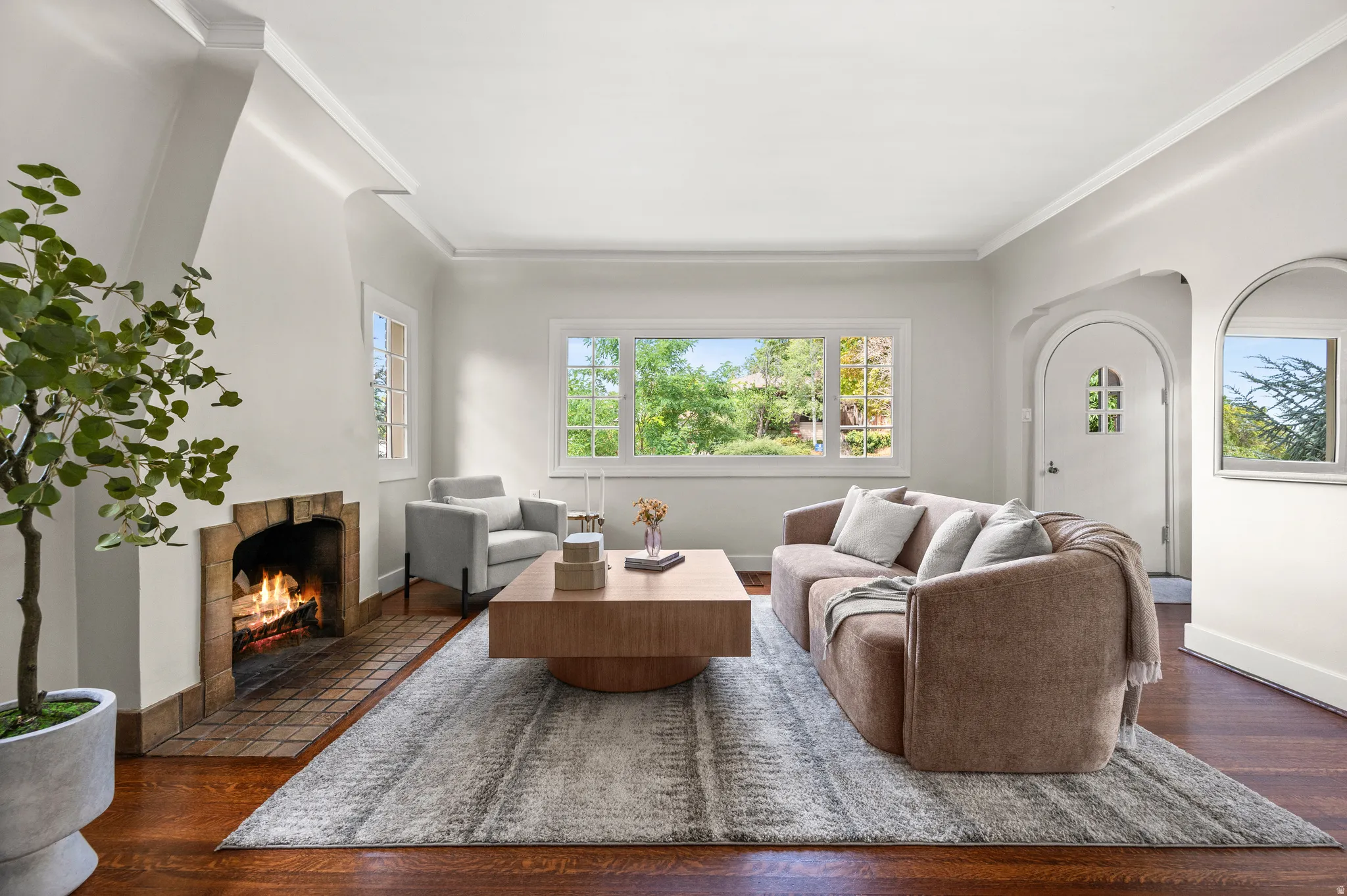 Spacious living room featuring a fireplace with brick hearth, hardwood flooring, multiple windows providing natural illumination, and an arched entryway