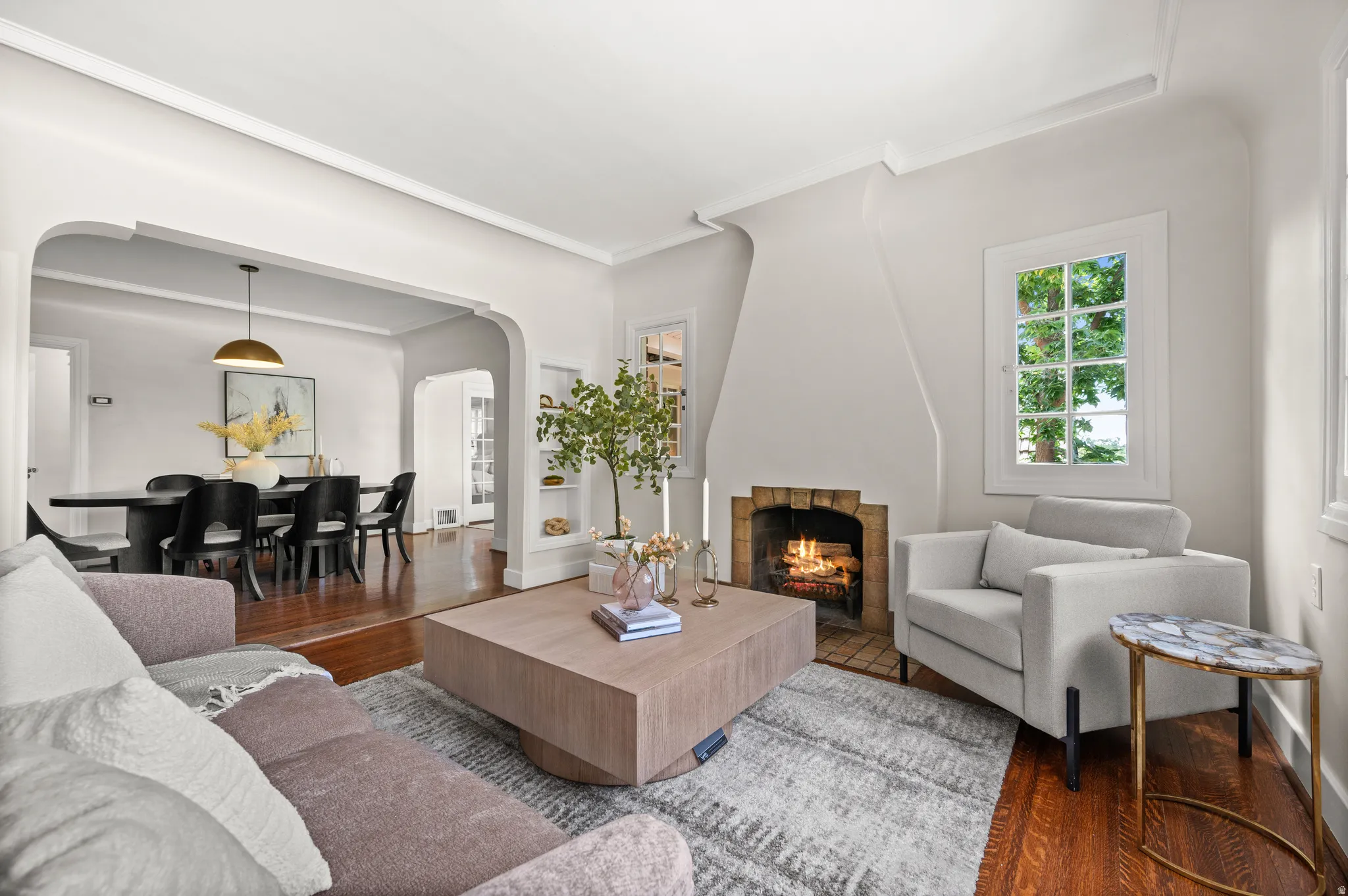 Living room featuring a prominent fireplace with a brick surround, hardwood flooring, and a large window with multiple panes