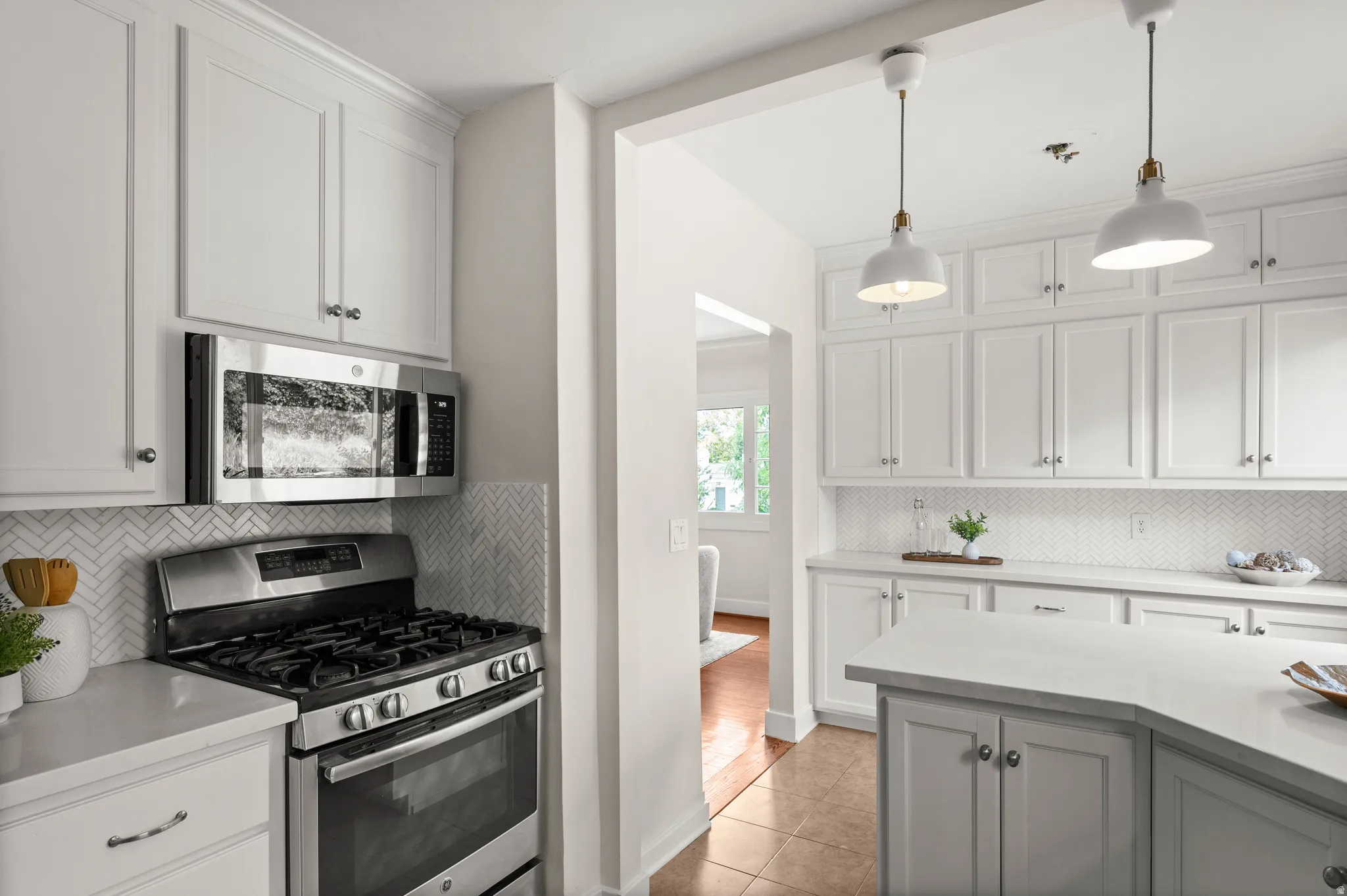 Kitchen featuring white shaker cabinetry, stainless steel appliances, herringbone tile backsplash, and light-toned countertops