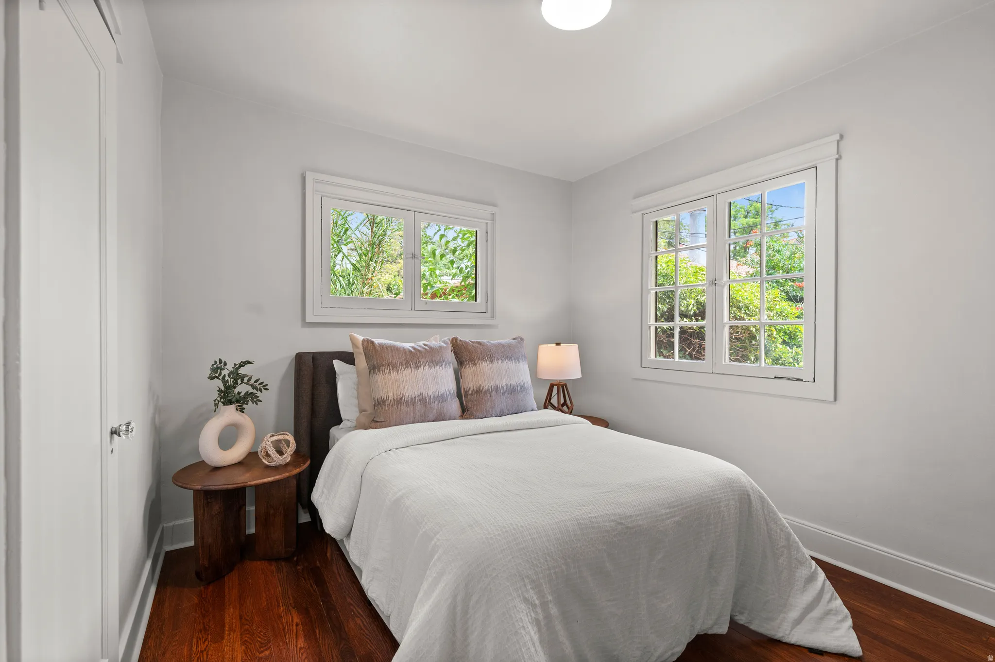 Light-filled room featuring two multi-pane windows, wood-finish flooring, white baseboards, and crown molding