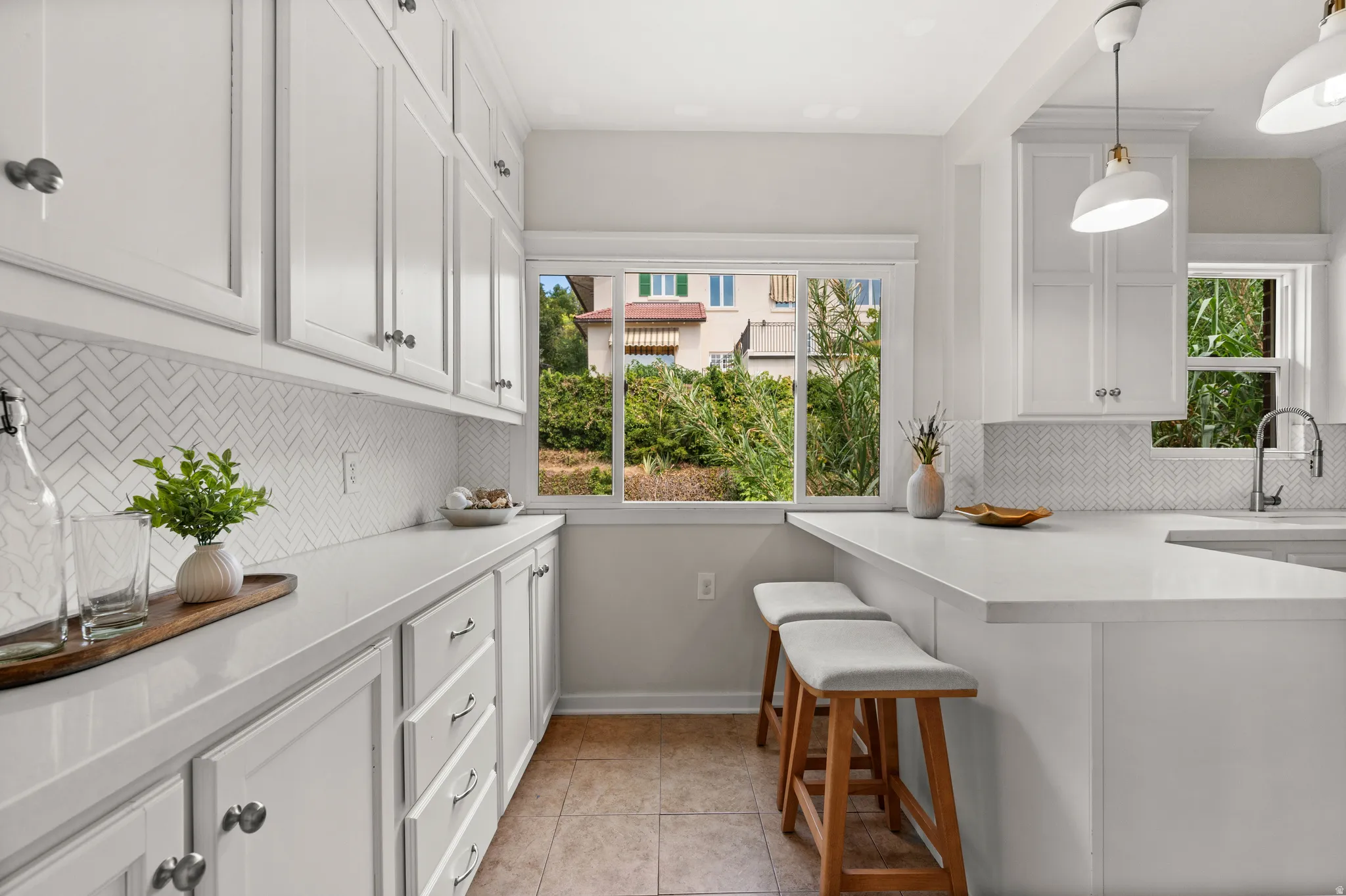 Kitchen featuring white shaker-style cabinetry, a white herringbone tile backsplash, and light-toned countertops