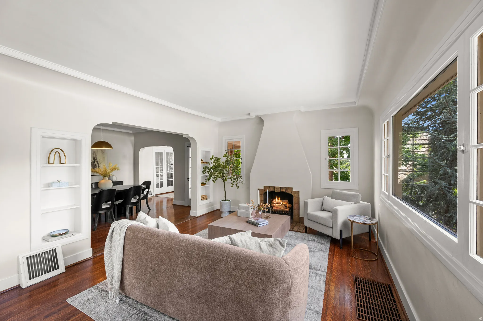 Hardwood flooring throughout the living area, featuring a fireplace with brick surround, built-in shelving, and large windows
