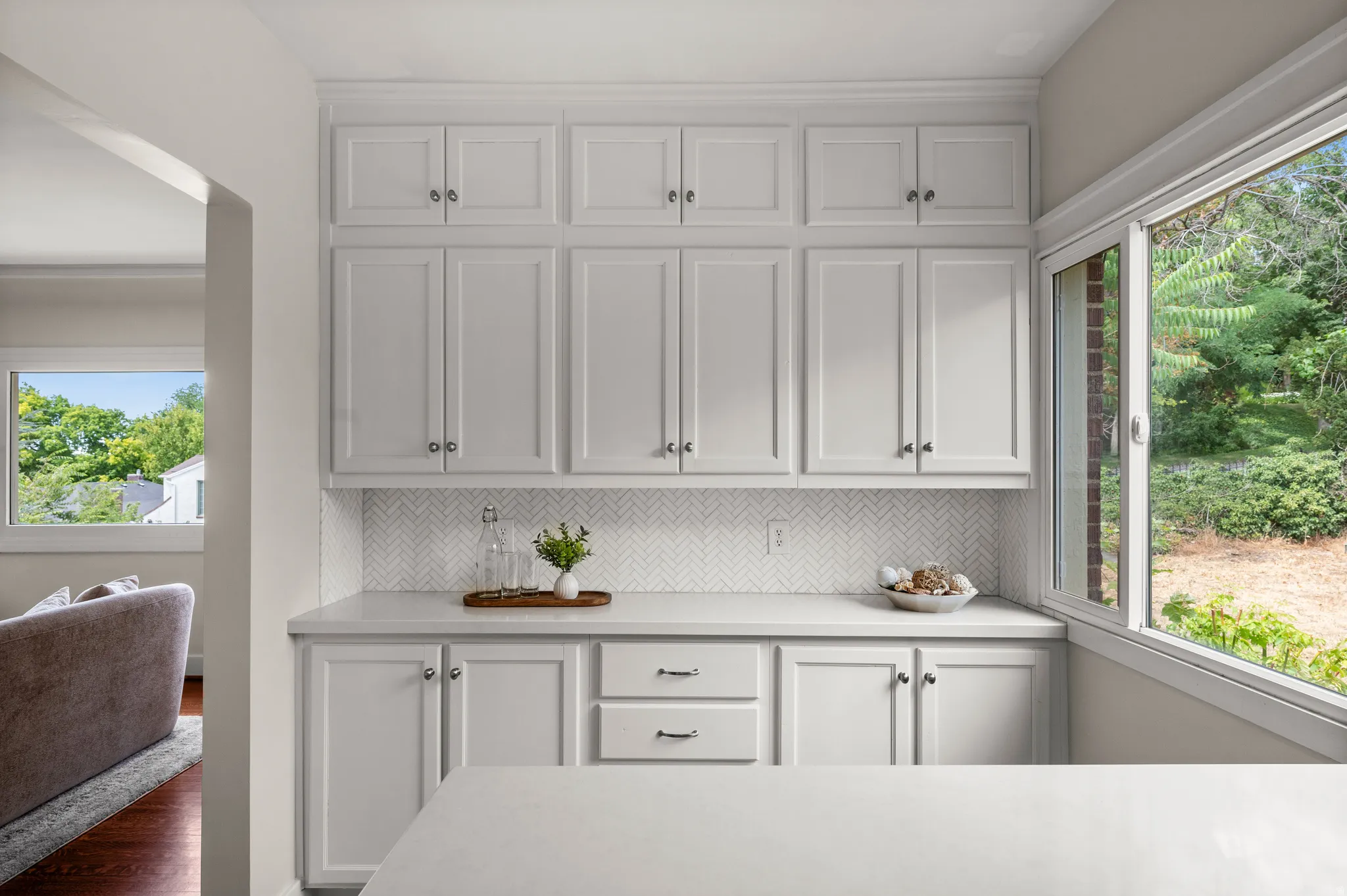 Extensive white cabinetry with crown molding, light-toned countertops, and a white herringbone tile backsplash