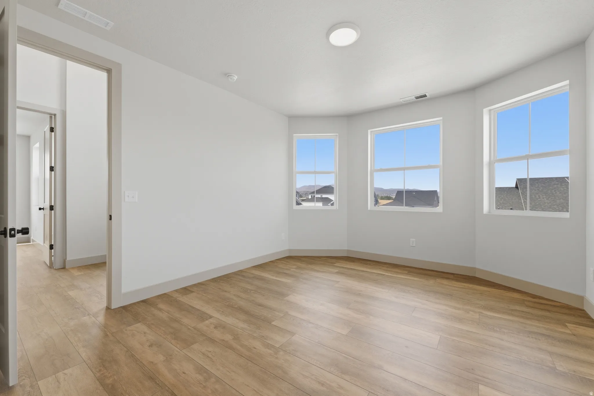 Spacious room featuring light wood-finish flooring and three large windows