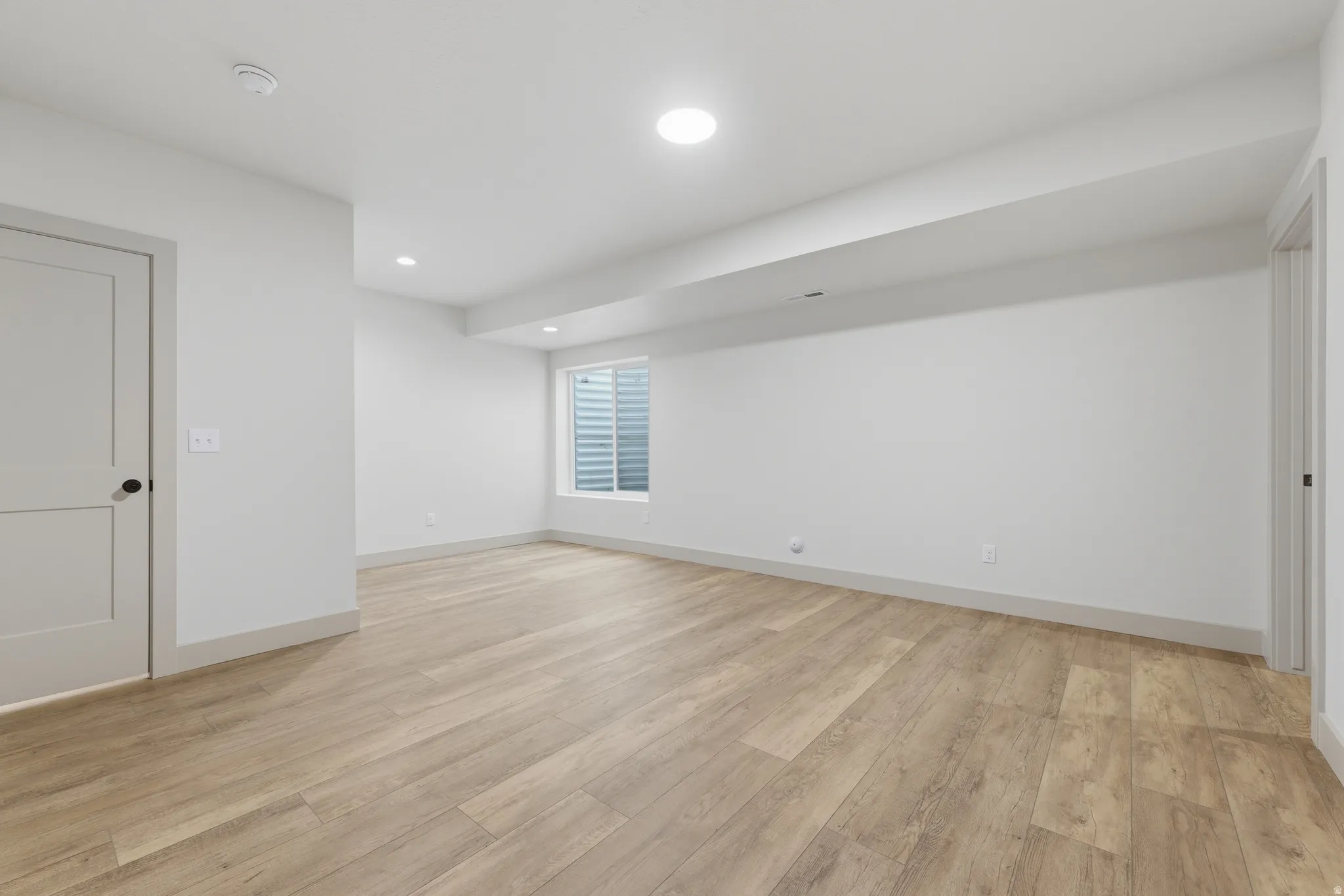 Expansive room featuring light wood-finish flooring, recessed lighting, and a window with a window well