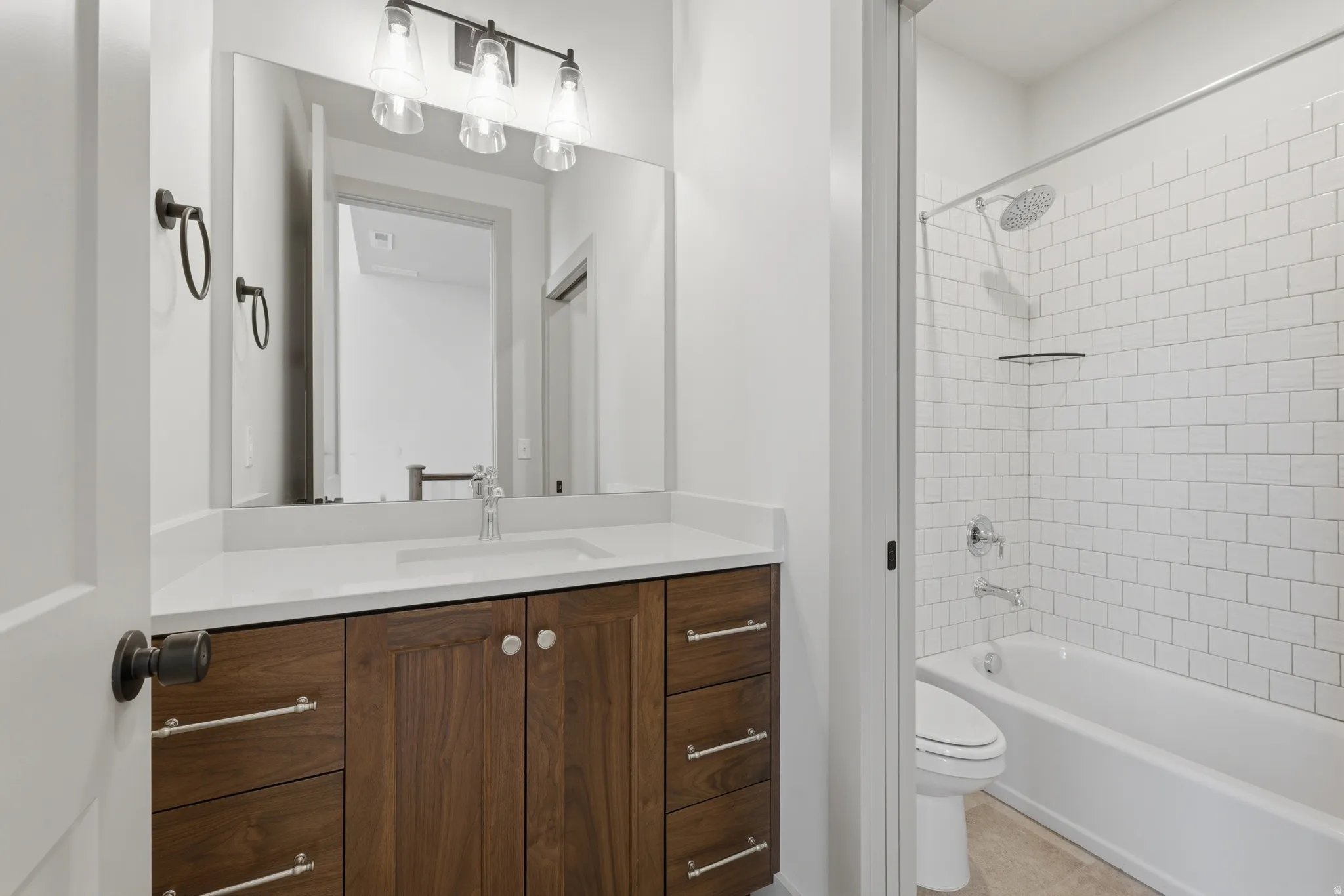 Bathroom featuring a wood-finish vanity with a light-toned countertop, an undermount sink, and a three-light fixture above a large mirror