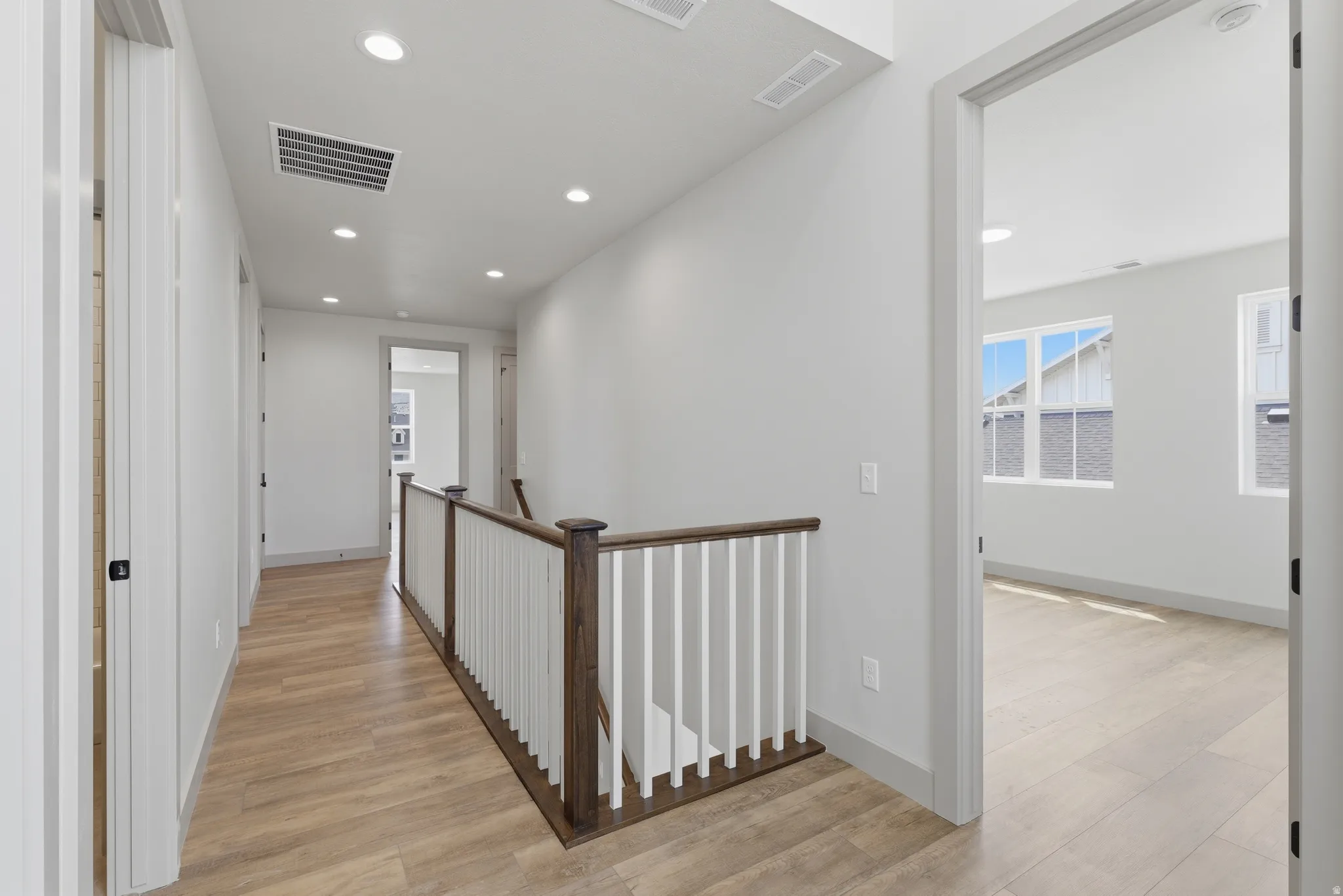 Upper-level hallway with wood-finish flooring, recessed lighting, and a white and dark wood banister
