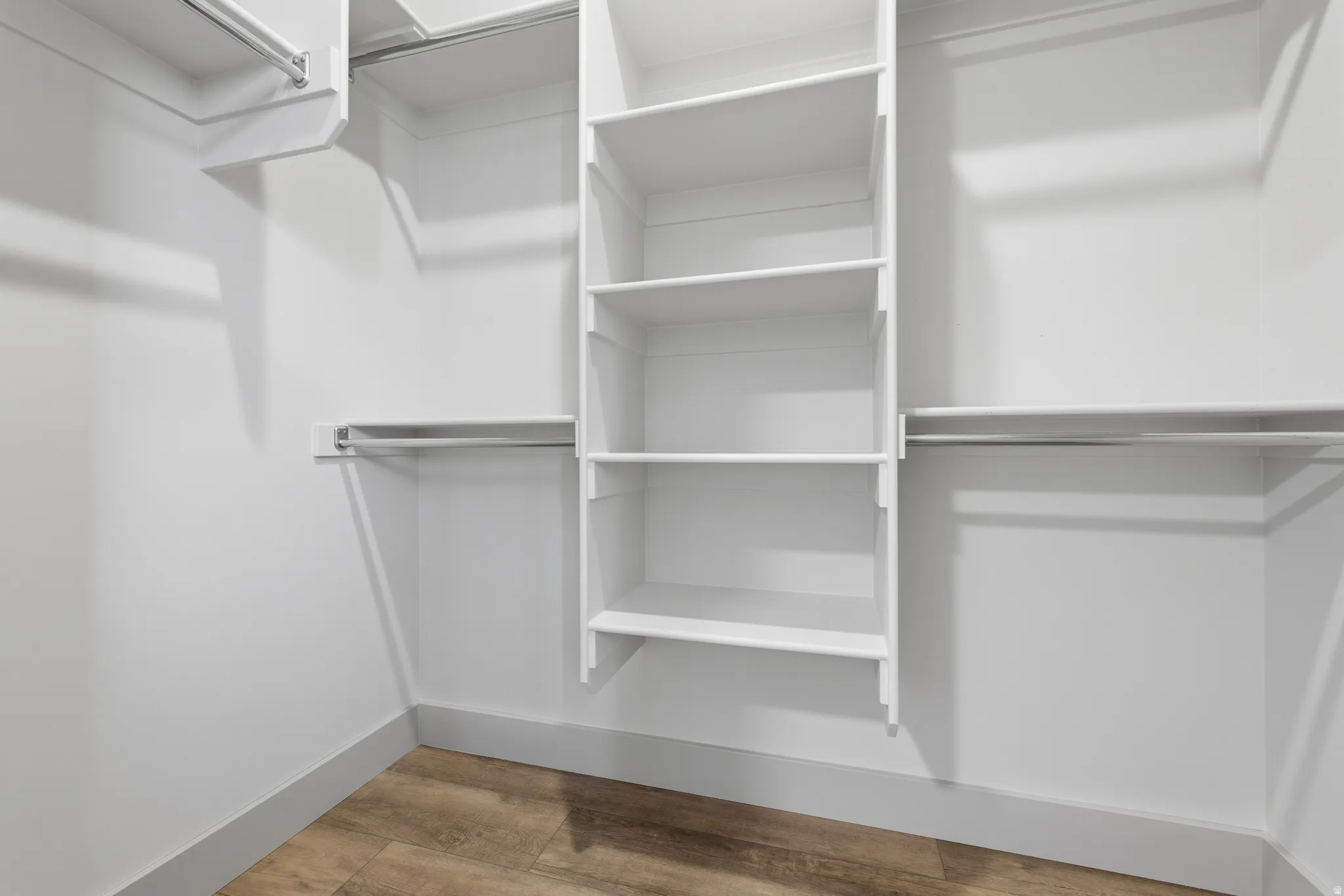 Walk-in closet featuring built-in shelving, multiple hanging rods, white walls, gray baseboards, and wood-finish flooring