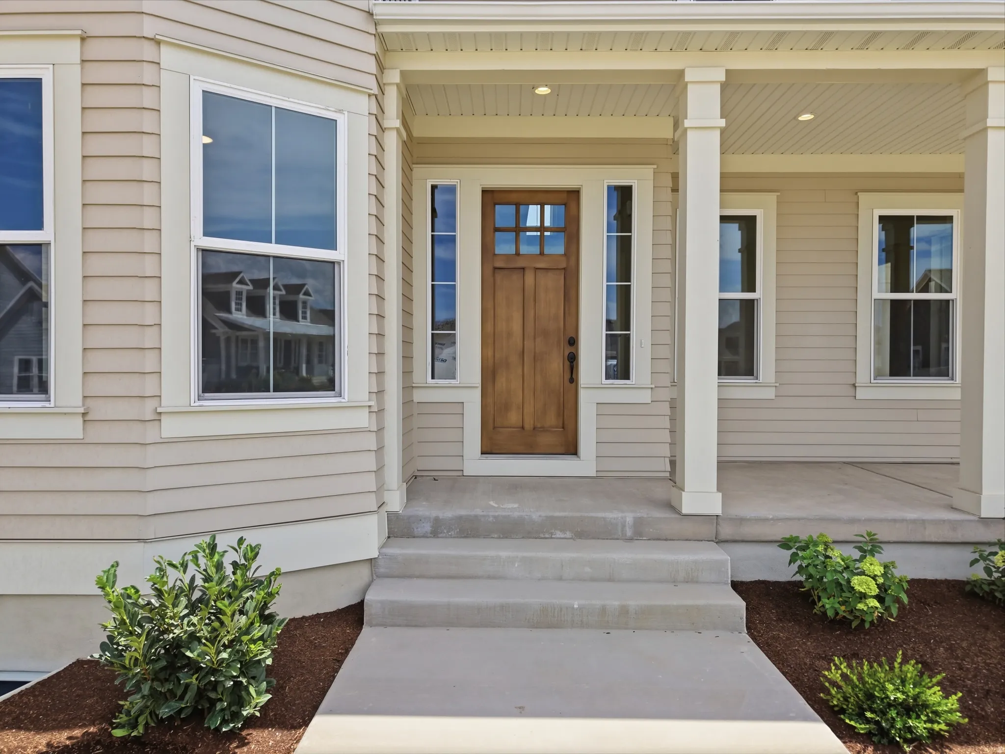 Covered front porch with a wood-finish entry door, sidelights, and a three-step concrete pathway