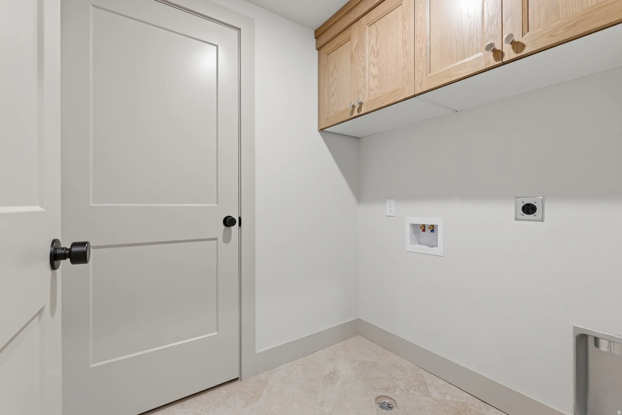 Laundry area with light wood-finish cabinetry, white flat-panel doors with matte black hardware, tile flooring, and clean white walls