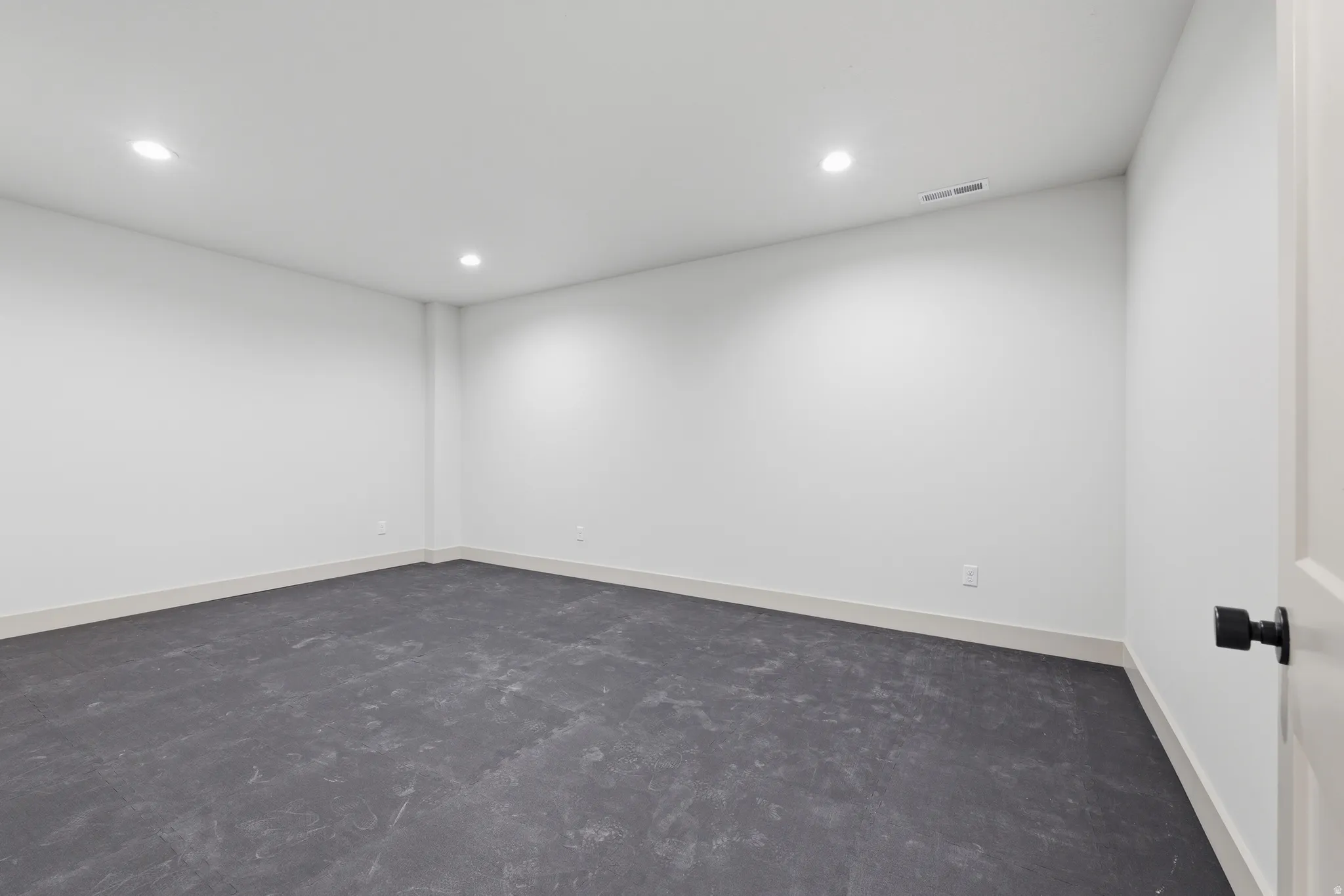 Spacious room featuring neutral white walls, recessed lighting, baseboard trim, and dark flooring