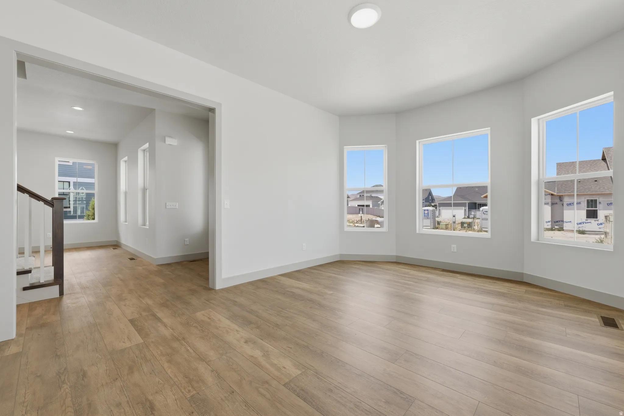 Open concept living space featuring wood-finish flooring, bright white walls, recessed lighting, and a bay window with three large windows