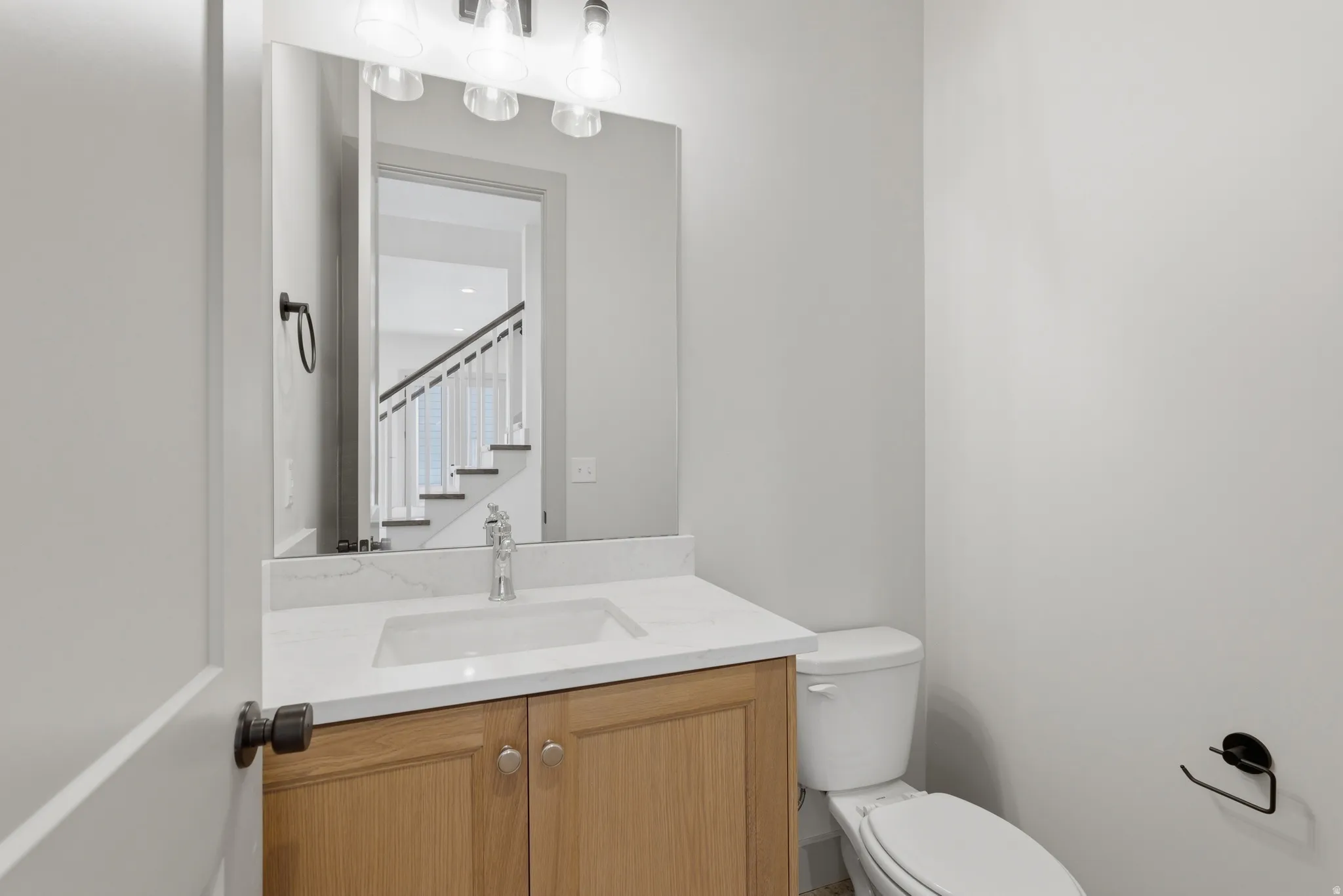 Bathroom featuring a light wood-finish vanity with a white countertop and undermount sink, a large wall-mounted mirror, and a white toilet