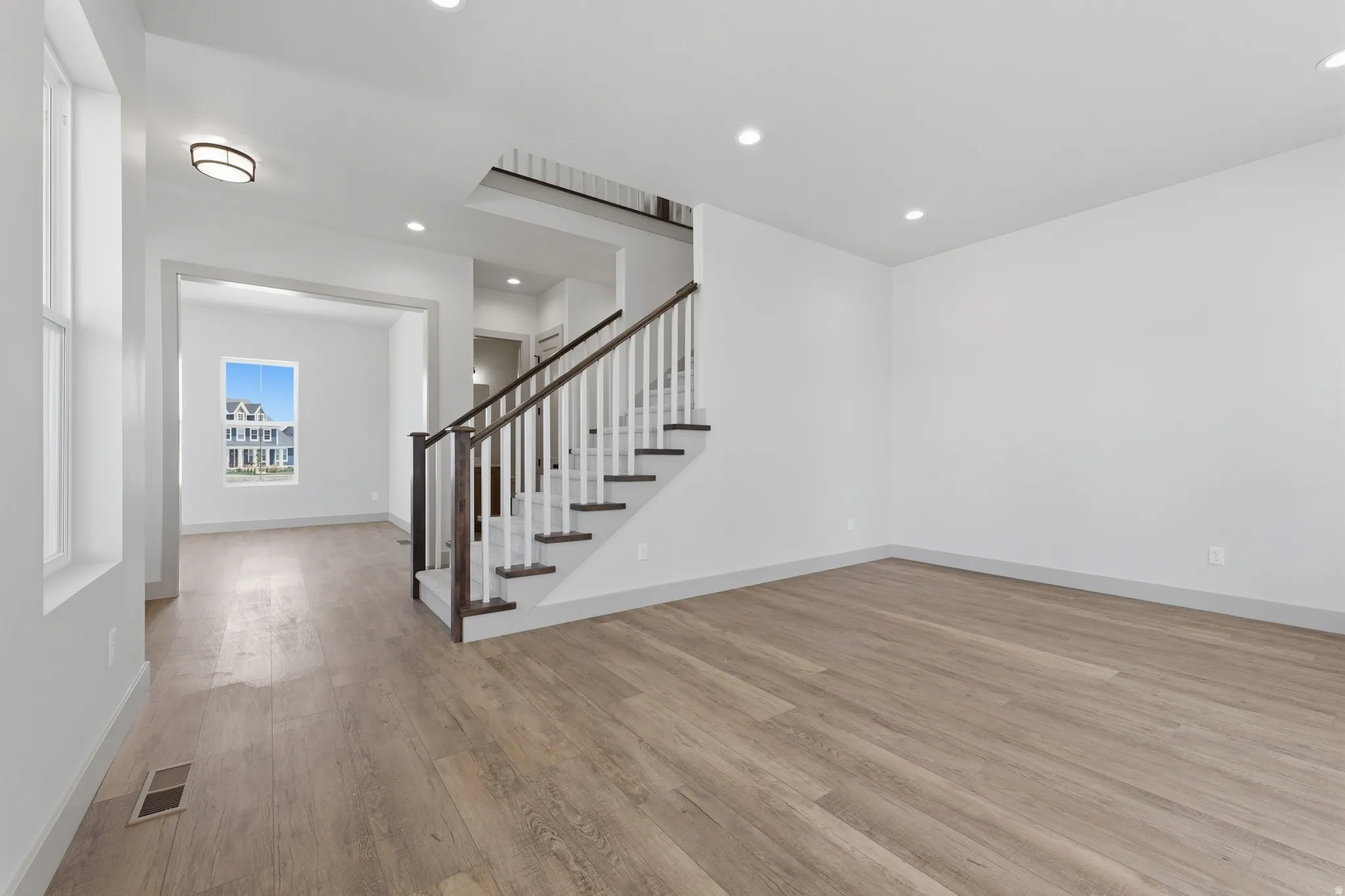 Spacious main living area featuring wide-plank wood-finish flooring, recessed lighting, and a contemporary staircase with dark wood handrails and white balusters