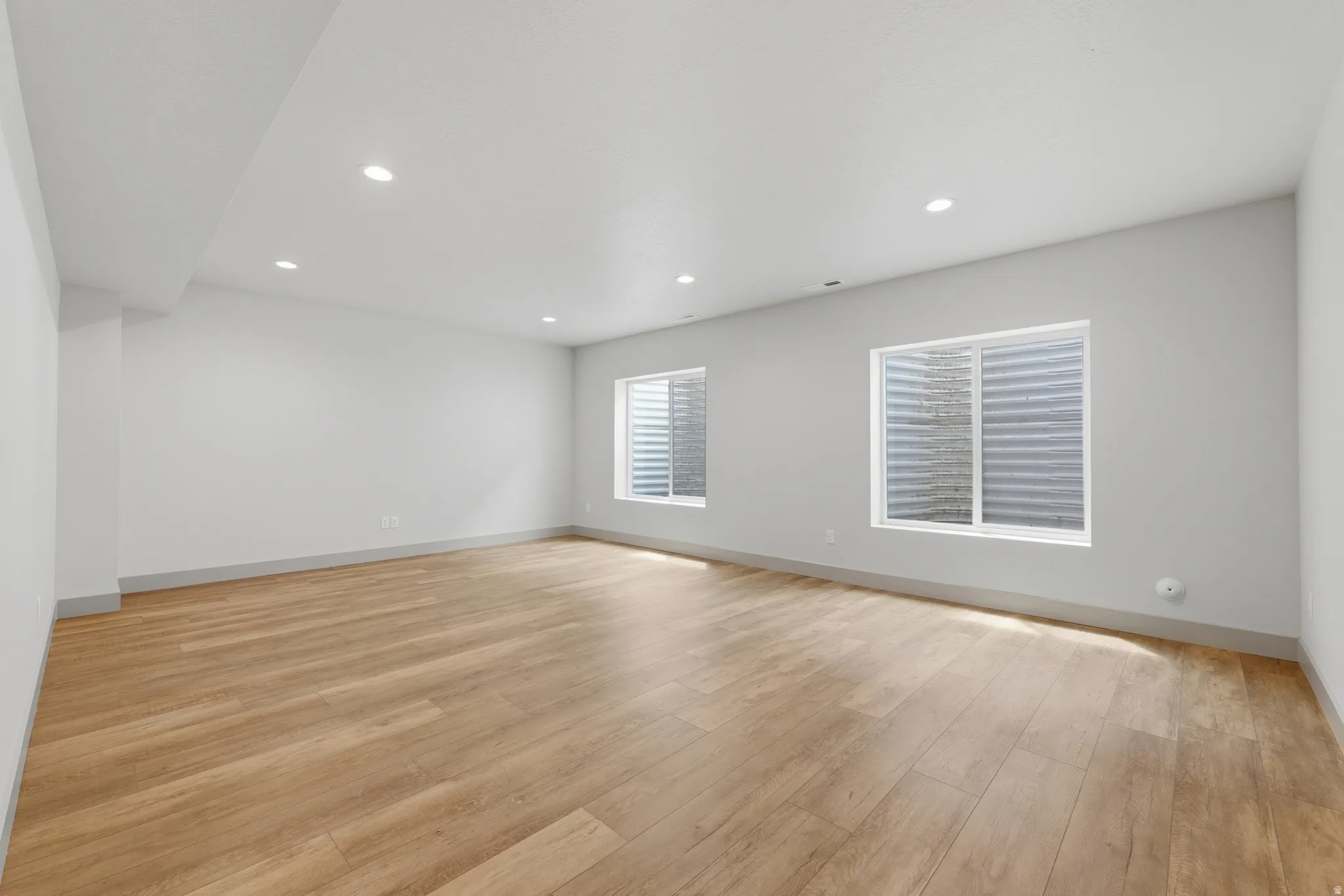 Spacious room featuring light wood-finish flooring and two egress windows