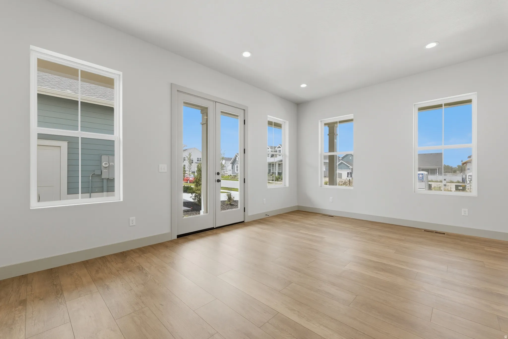 Spacious room featuring wood-finish flooring, light gray walls, recessed lighting, multiple windows, and French doors
