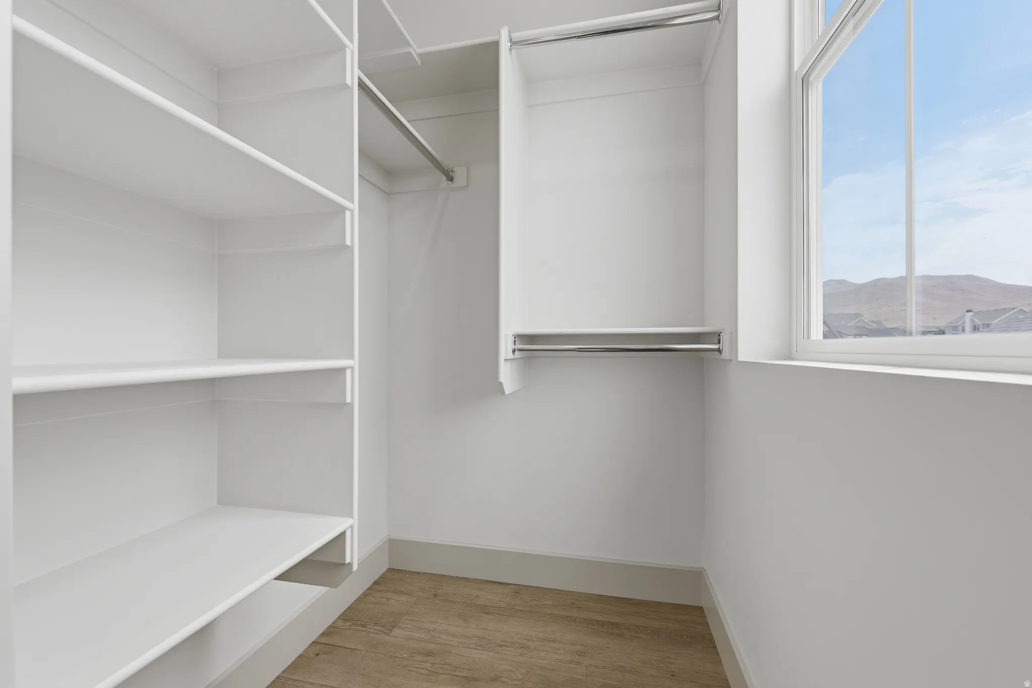 Walk-in closet featuring built-in shelving, chrome hanging rods, a double-hung window, and wood-finish flooring
