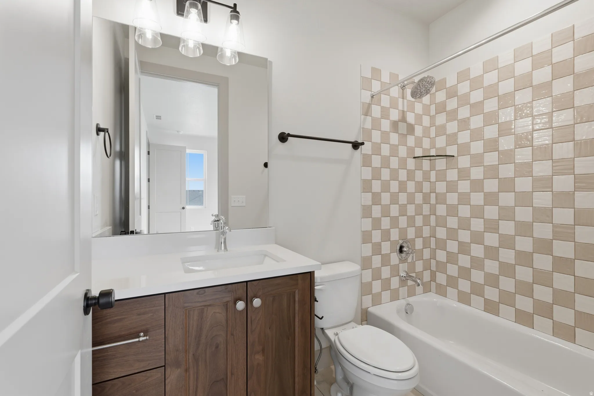 teen Suite ensuite bathroom. Bathroom featuring a wood-finish vanity with a white countertop and integrated sink, a large mirror, and a shower/tub combination with checkered tile surround