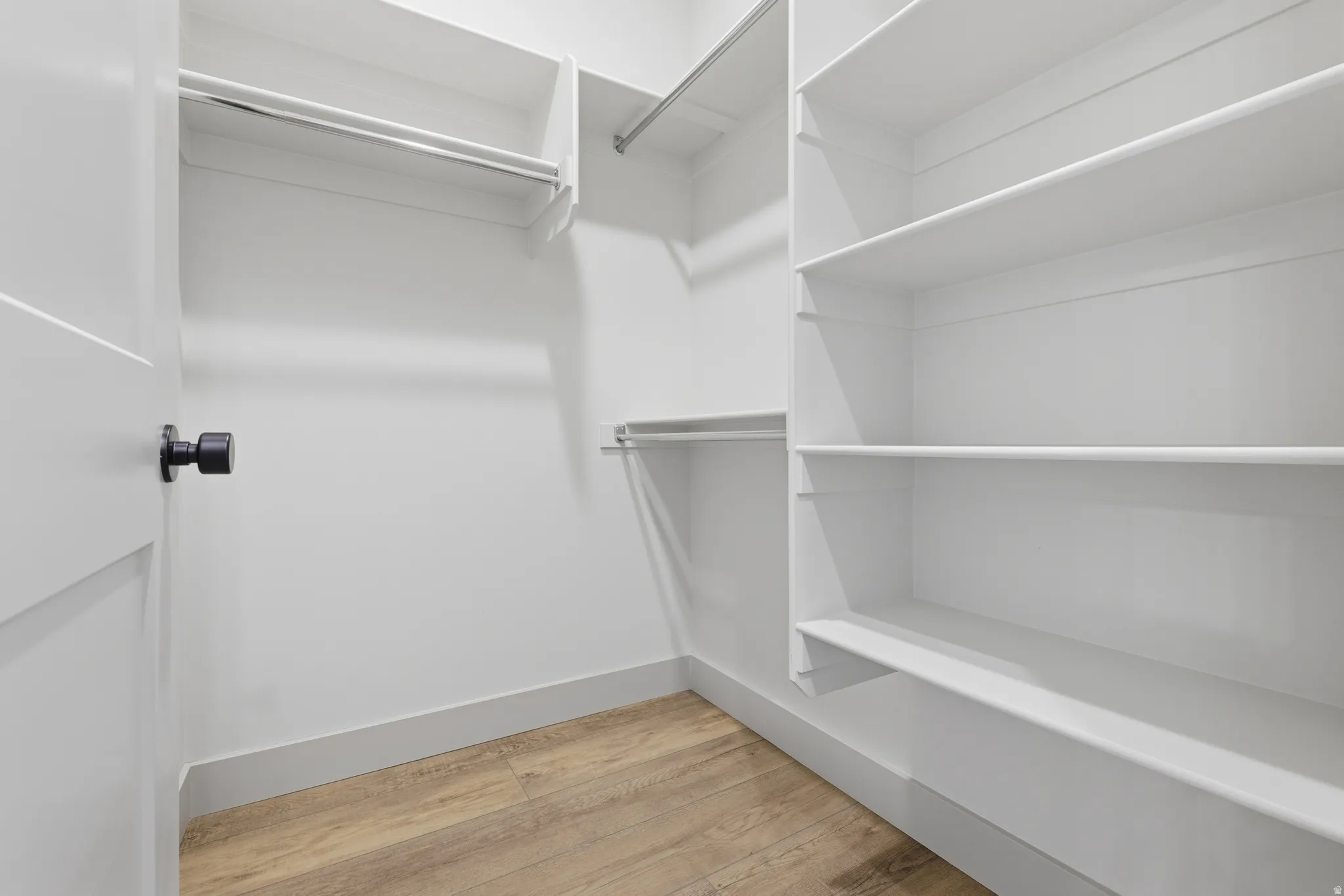 Walk-in closet with integrated shelving, multiple hanging rods, and wood-finish flooring