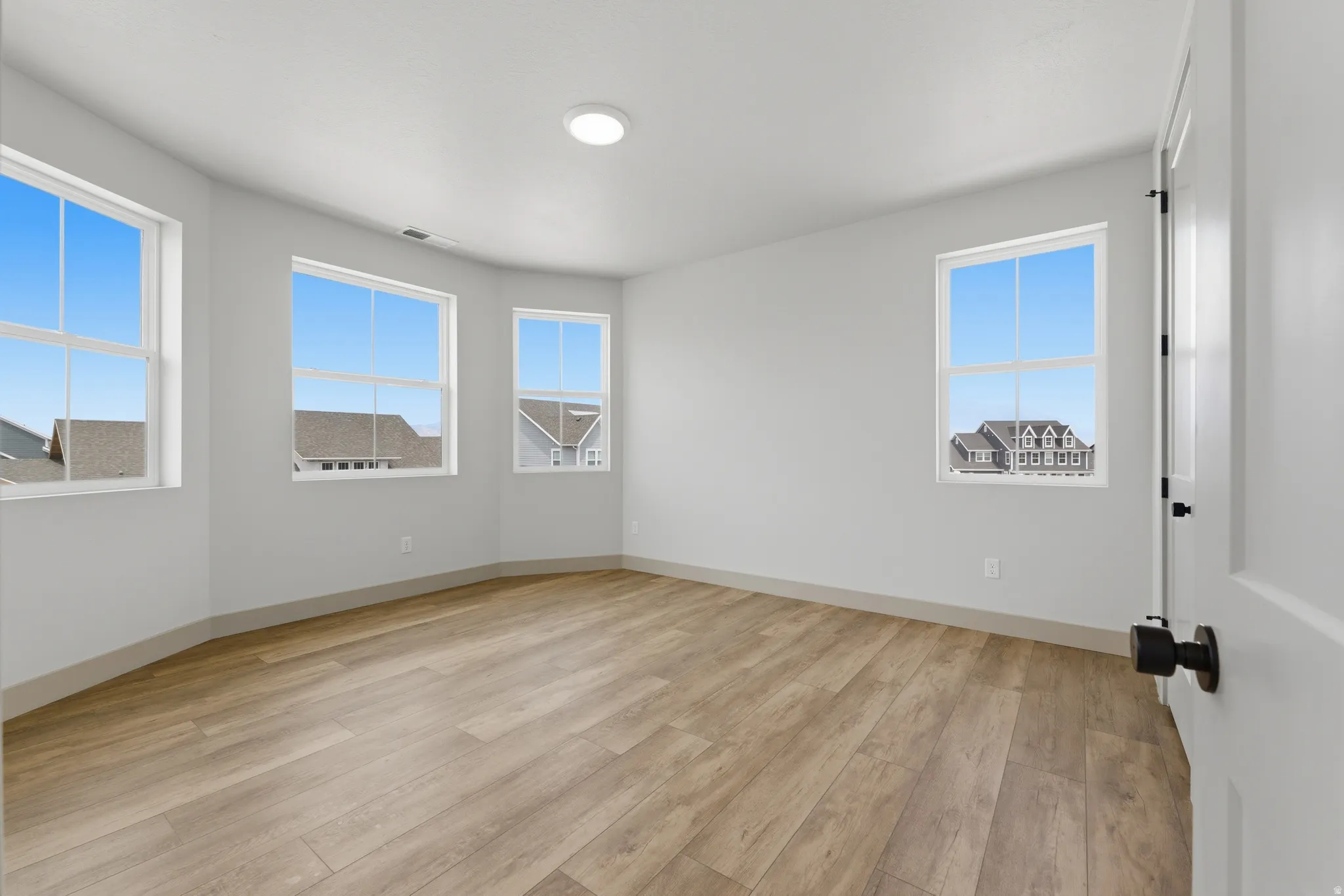Spacious room featuring light wood-finish flooring, white walls, and a curved architectural element with a multi-pane window configuration