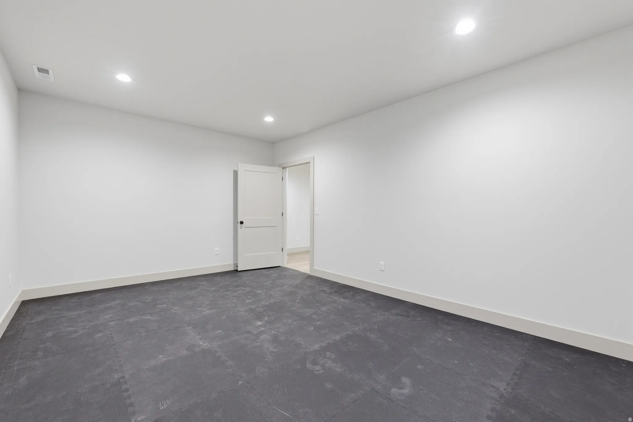 Spacious room featuring neutral white walls, recessed ceiling lighting, and a durable dark-toned floor
