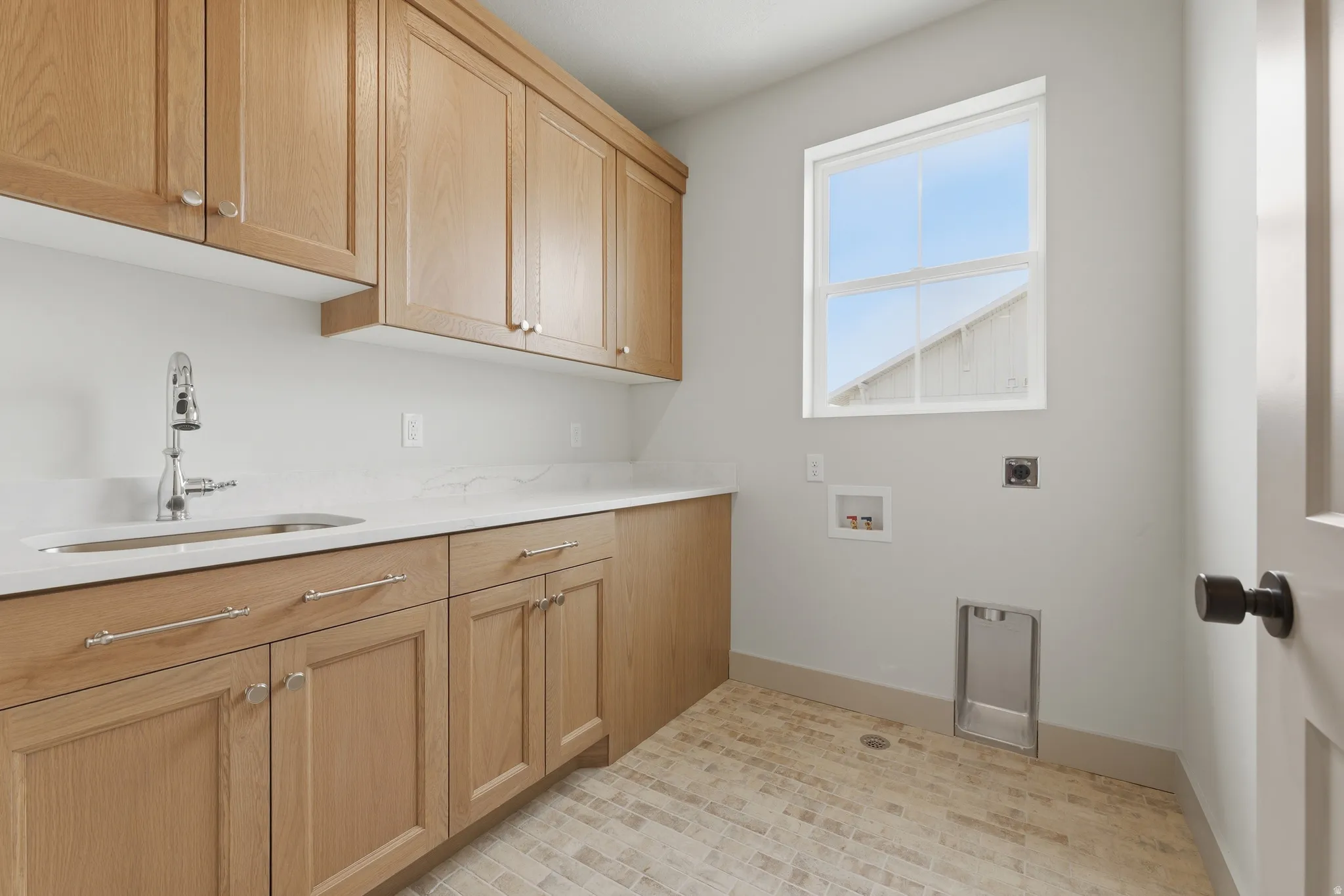Utility room featuring wood cabinetry, white stone countertops, a stainless steel sink with a chrome faucet, a window, and tile flooring