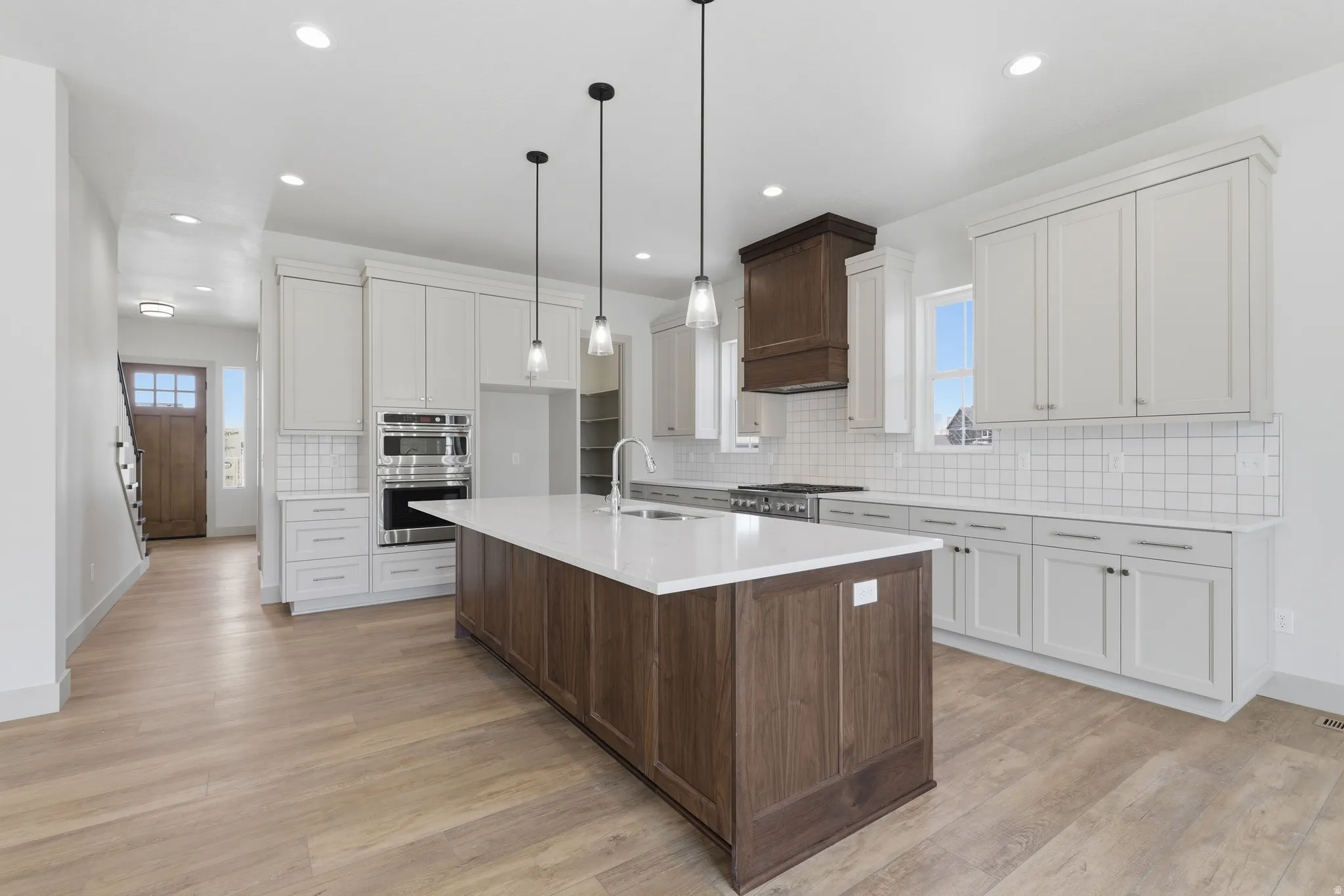 Spacious kitchen featuring an expansive center island with a white countertop, two-tone cabinetry, stainless steel appliances, and wood-finish flooring