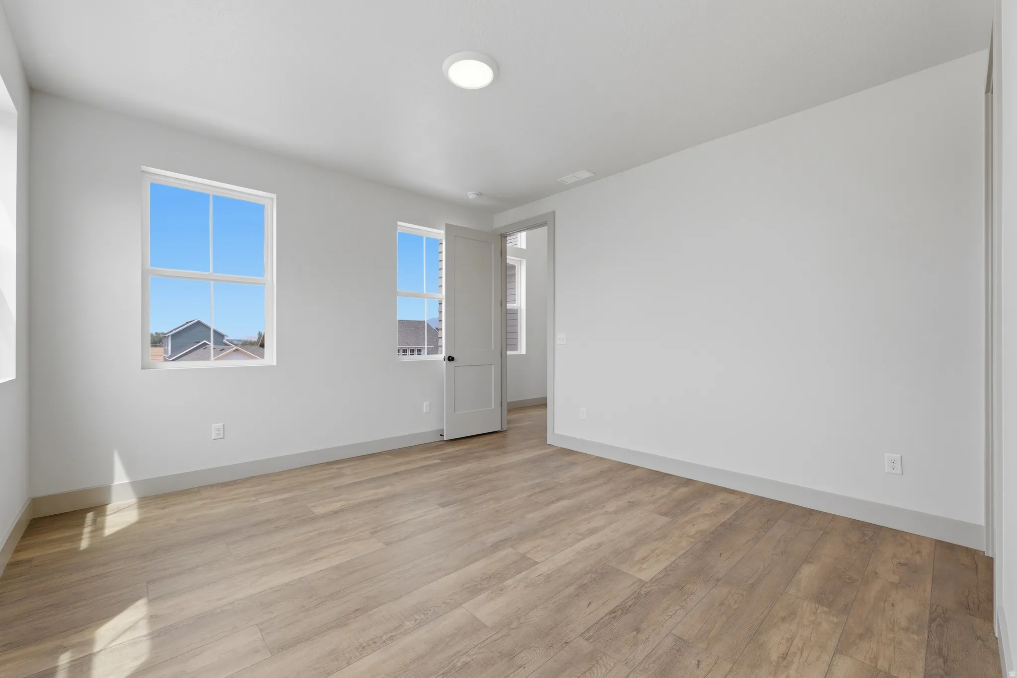 Spacious room featuring light wood-finish flooring, white walls, and multiple large windows