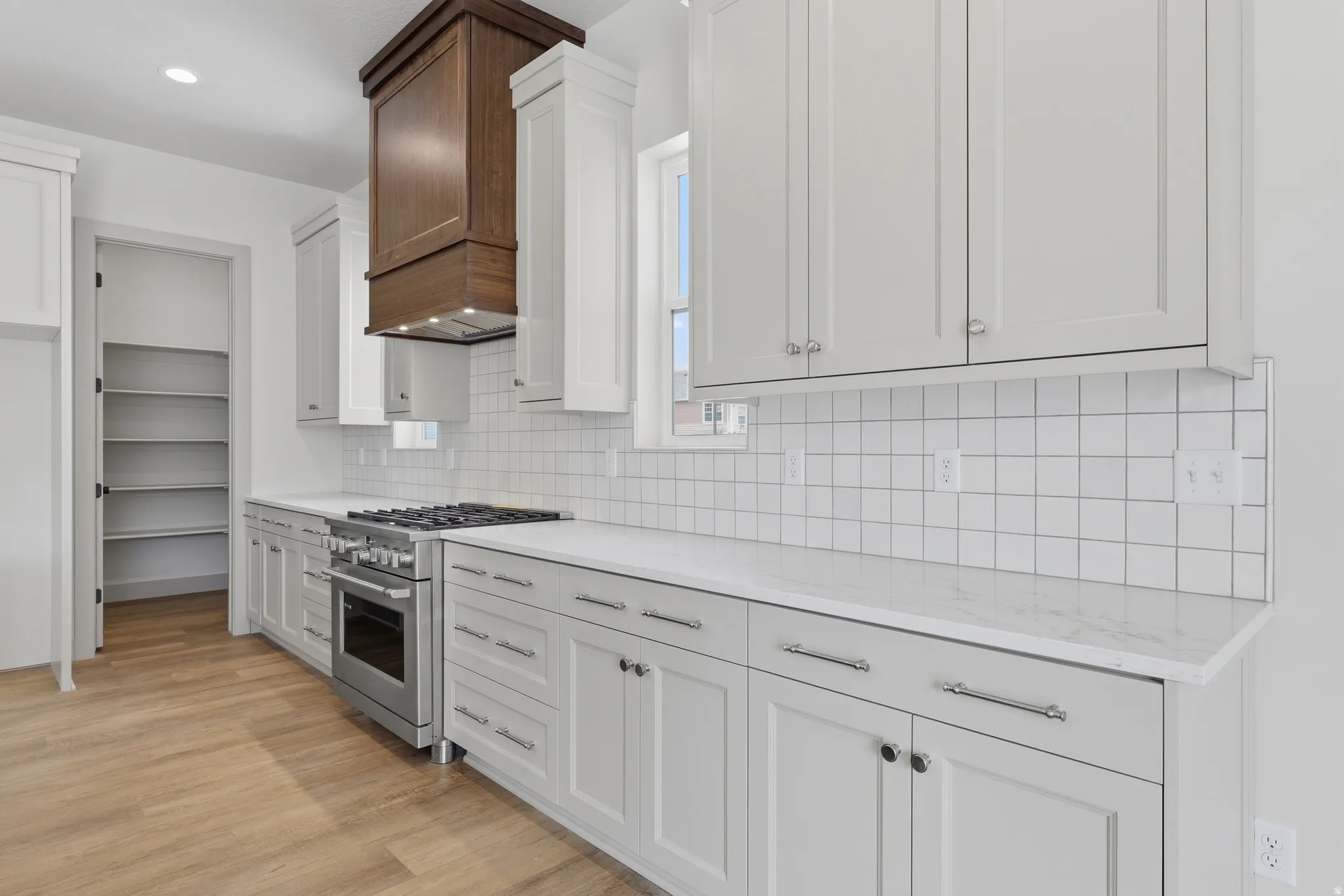 Kitchen featuring a stainless steel range oven, a coordinating wood-paneled range hood, and light wood-finish flooring